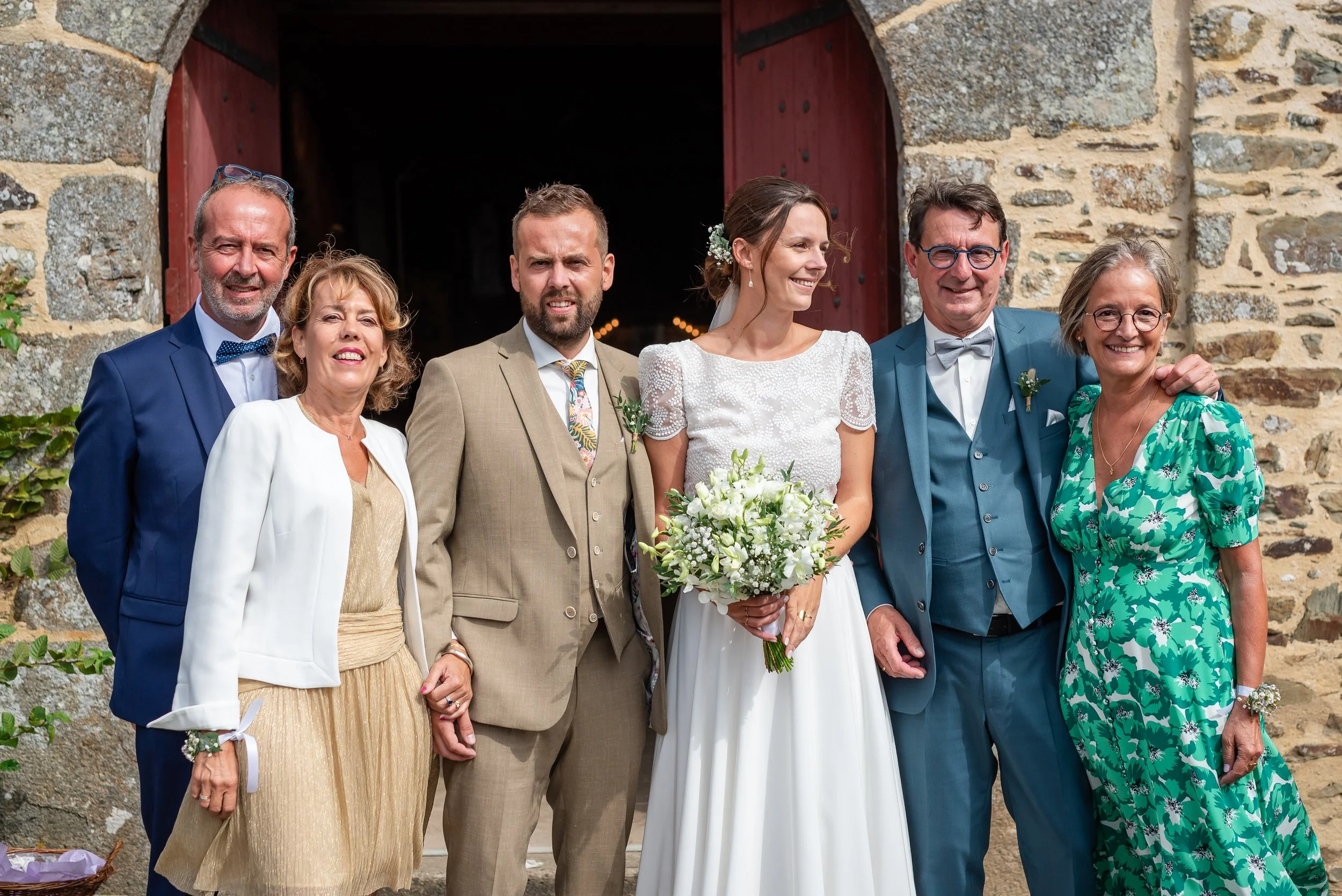 Groupe de personnes posant devant une vieille porte en pierre pour un mariage, avec la mariée en robe blanche au centre, entourée de membres de la famille.