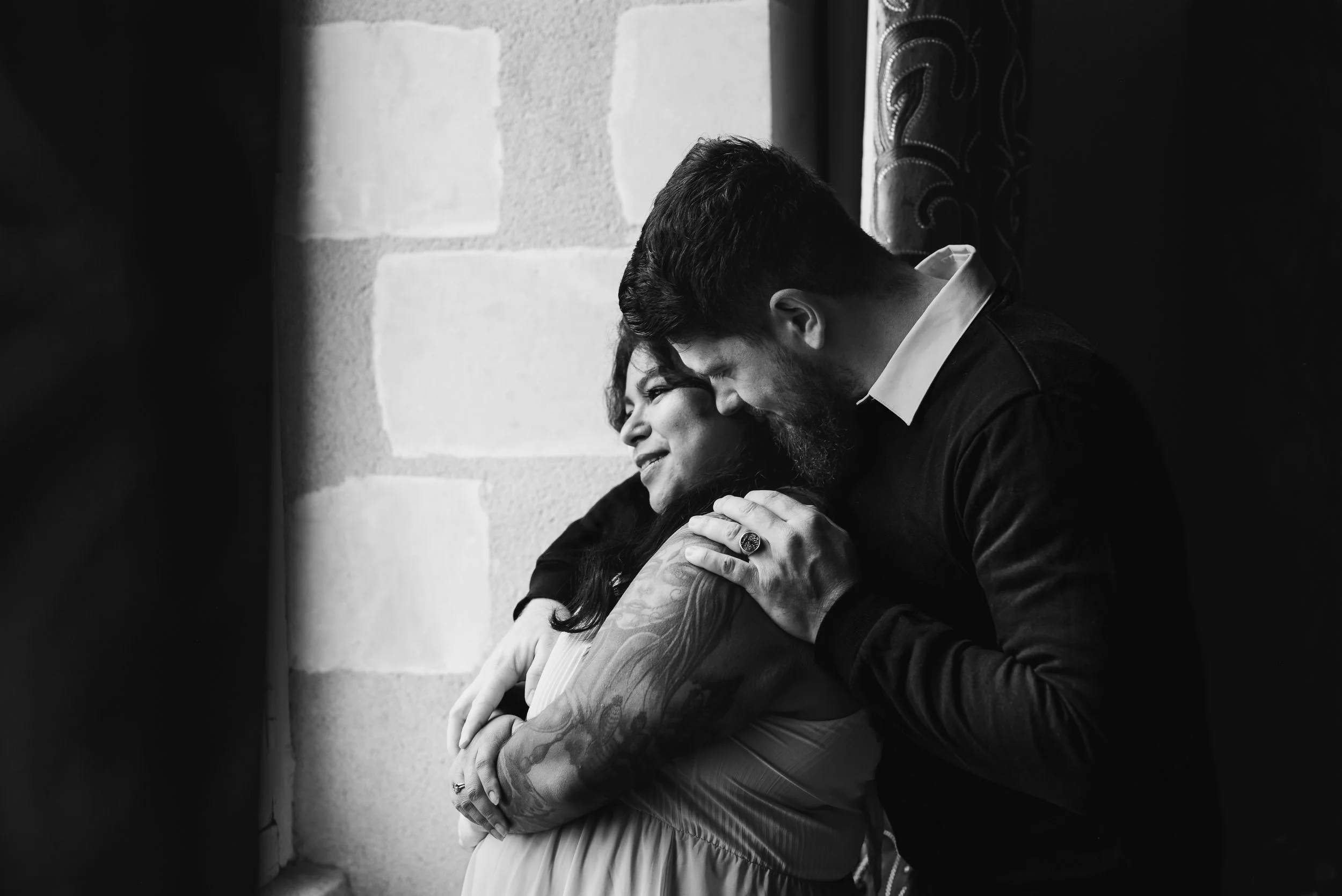 Deux personnes s'embrassent tendrement, un homme avec une barbe et une femme tatouée, dans un cadre intérieur en noir et blanc.