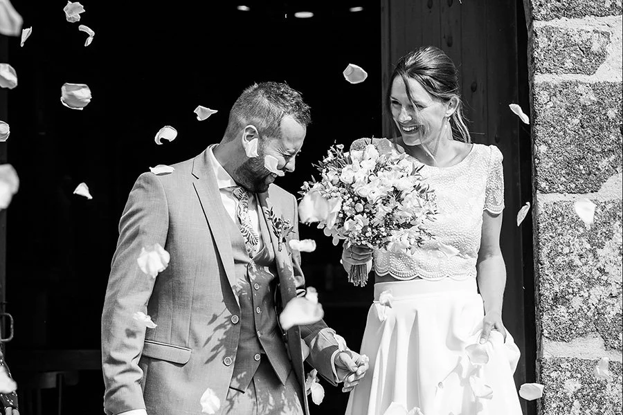 Un couple de mariés souriant, entouré de pétales de rose en suspension, lors de leur mariage.