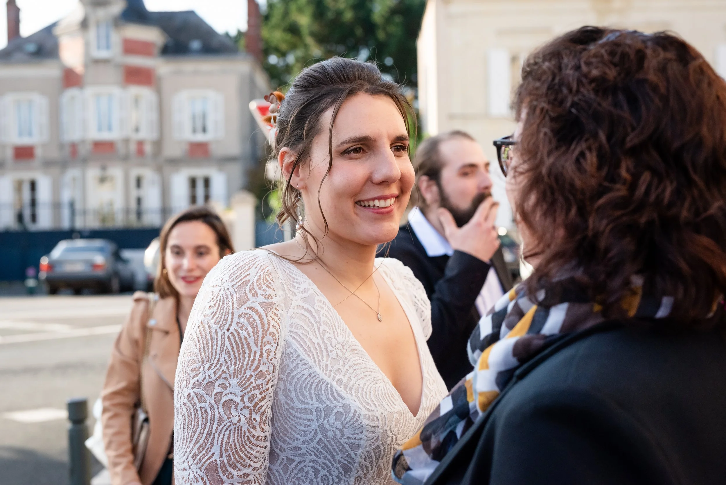 Jeune femme souriante discutant avec une autre personne lors d'un événement en plein air, avec d'autres personnes en arrière-plan. Lieu urbain avec des bâtiments en arrière-plan.