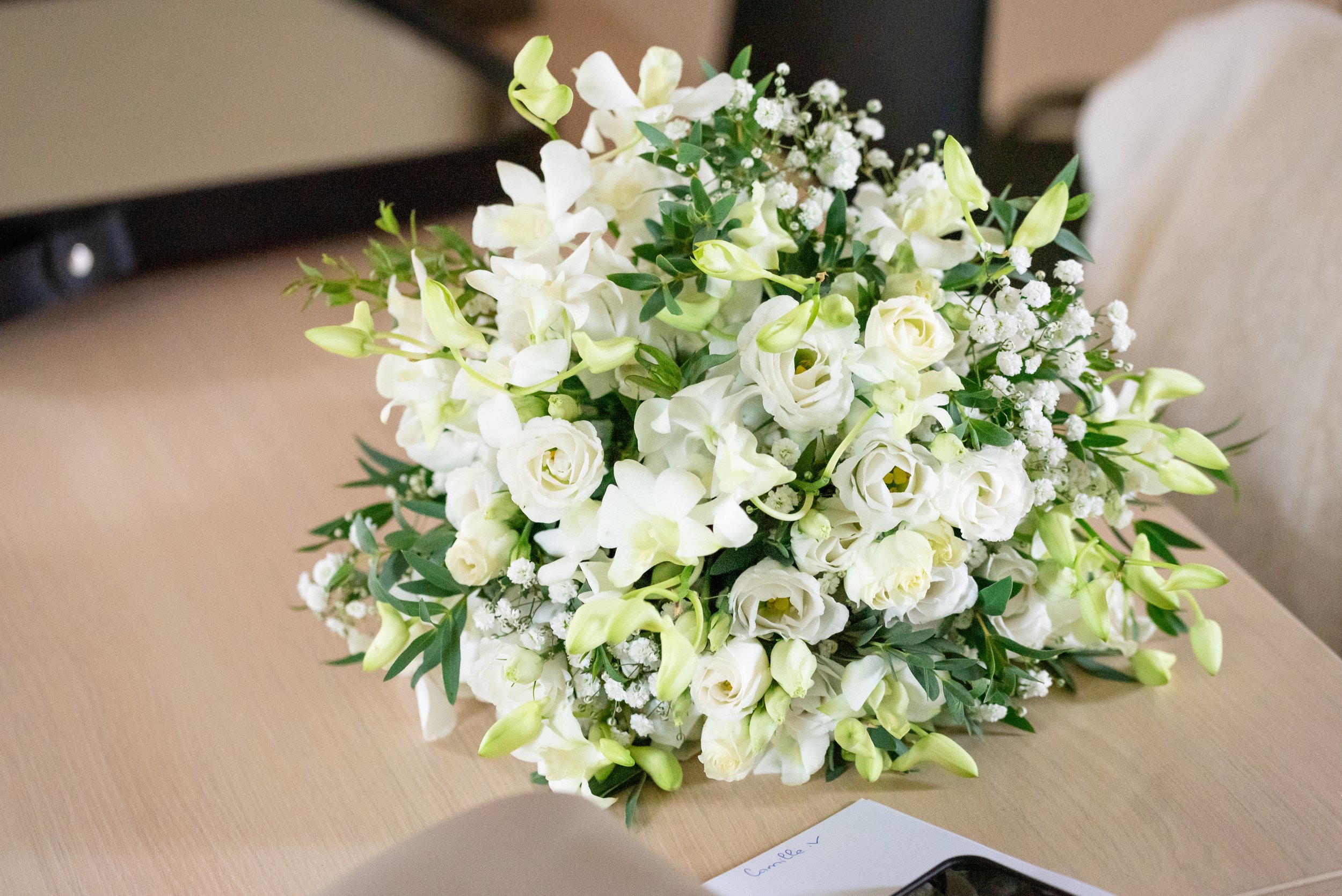 Un bouquet de fleurs blanches, comprenant des roses, des lisianthus et des gypsophiles, posé sur une table en bois