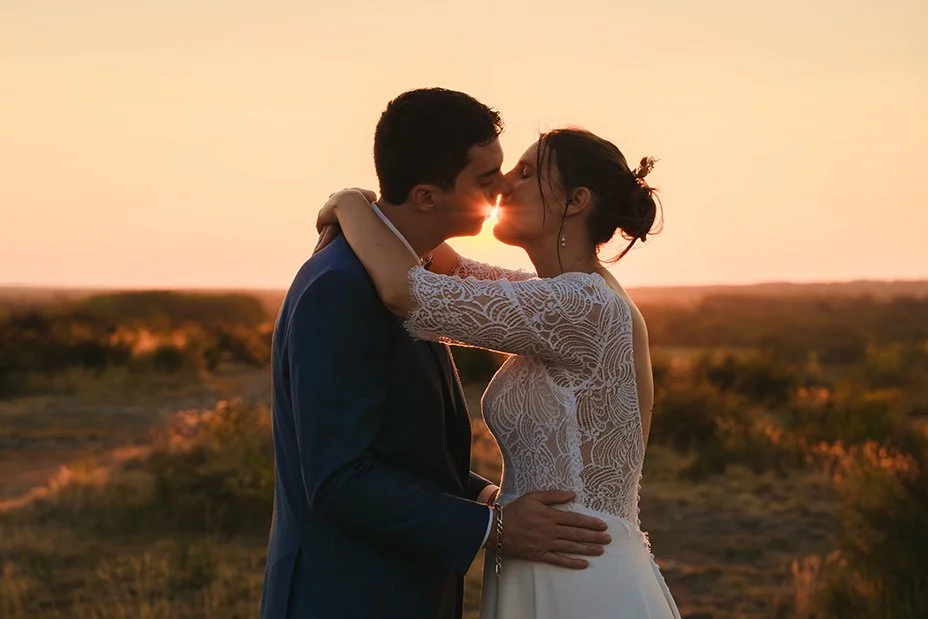Un couple marié s'embrasse lors d'un coucher de soleil dans un paysage naturel.