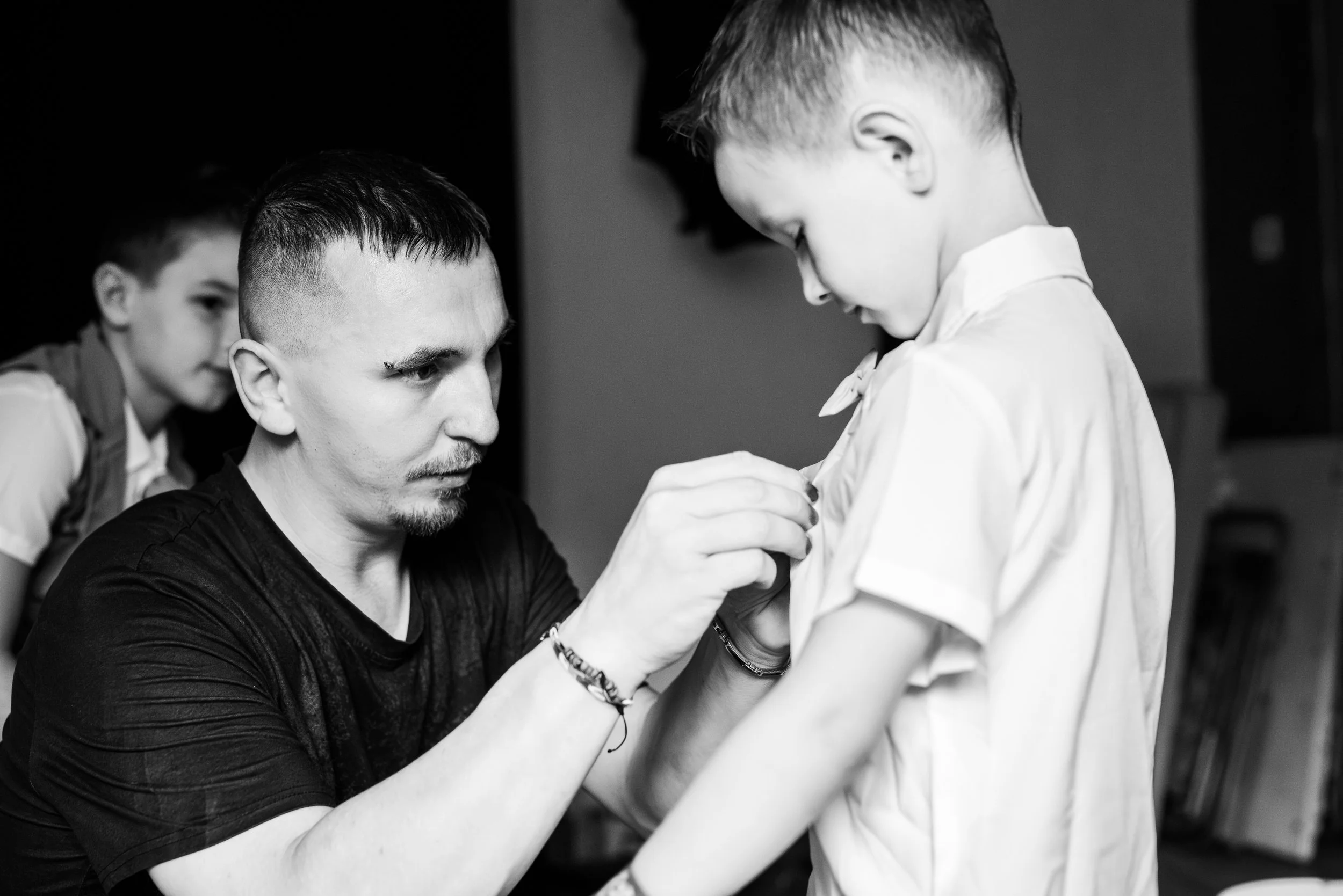 Un homme aide une jeune fille à boutonner sa chemise, en noir et blanc.
