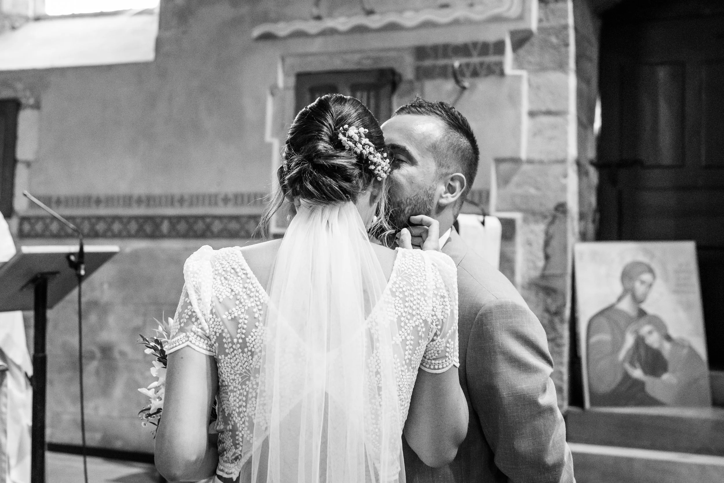 Un couple de mariés s'embrassant lors de leur mariage dans une église, en noir et blanc.