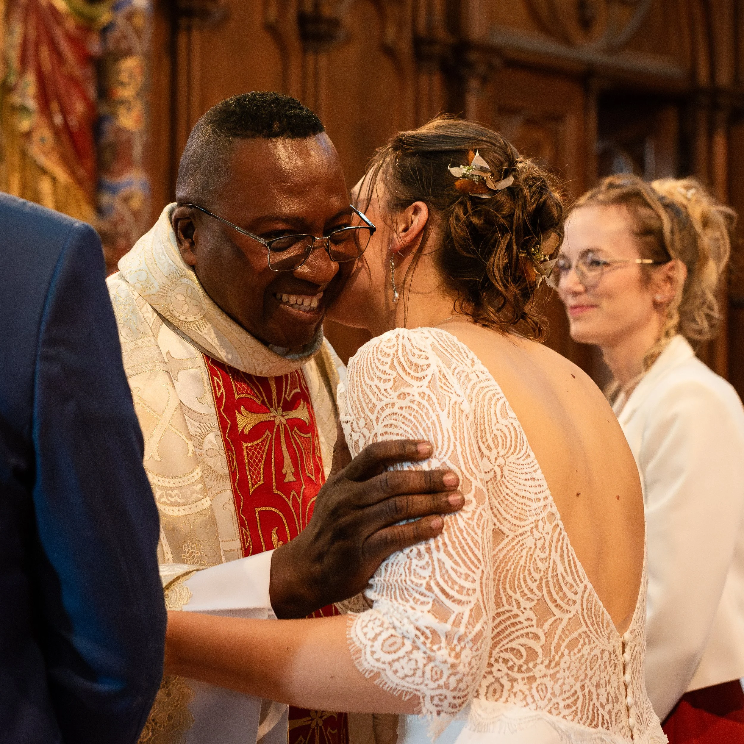 Un homme et une femme lors d'une cérémonie ou célébration, l'homme porte des vêtements brodés dorés et un cercle de médailles, la femme porte une robe en dentelle et une coiffe décorée de plumes et de fleurs.