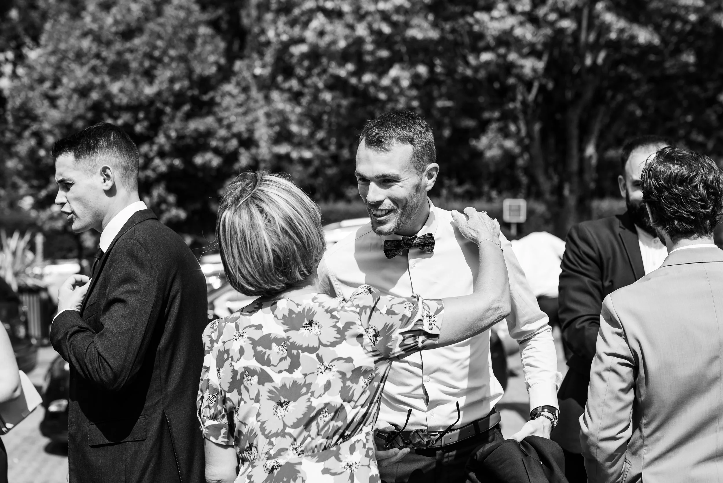 Groupe de personnes habillées formellement, partageant un moment convivial en extérieur, lors d'un événement en journée.