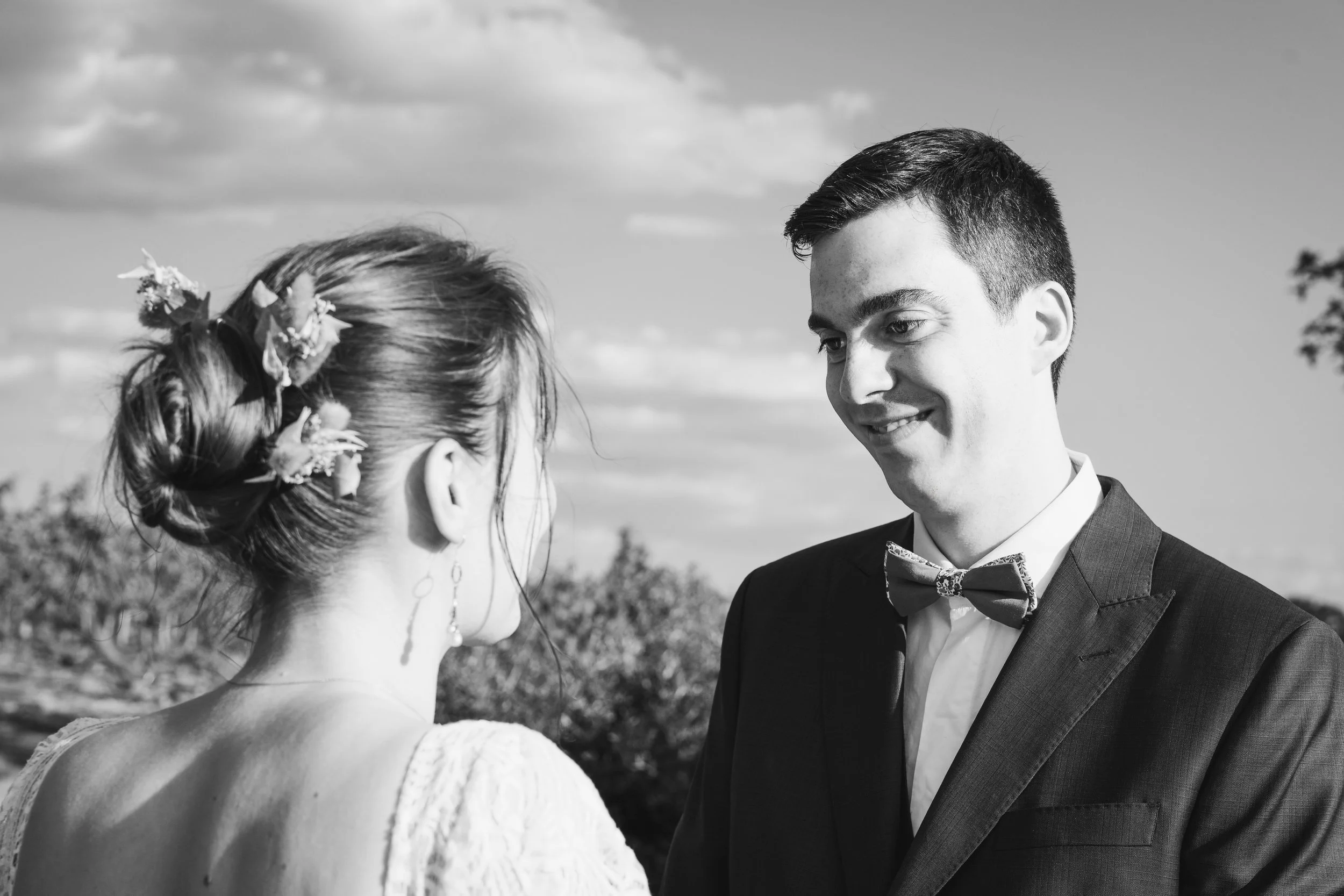 Un homme et une femme regardent l'un l'autre lors d'une rencontre extérieure, l'homme porte un costume et un nœud papillon, la femme a des cheveux coiffés avec des fleurs.
