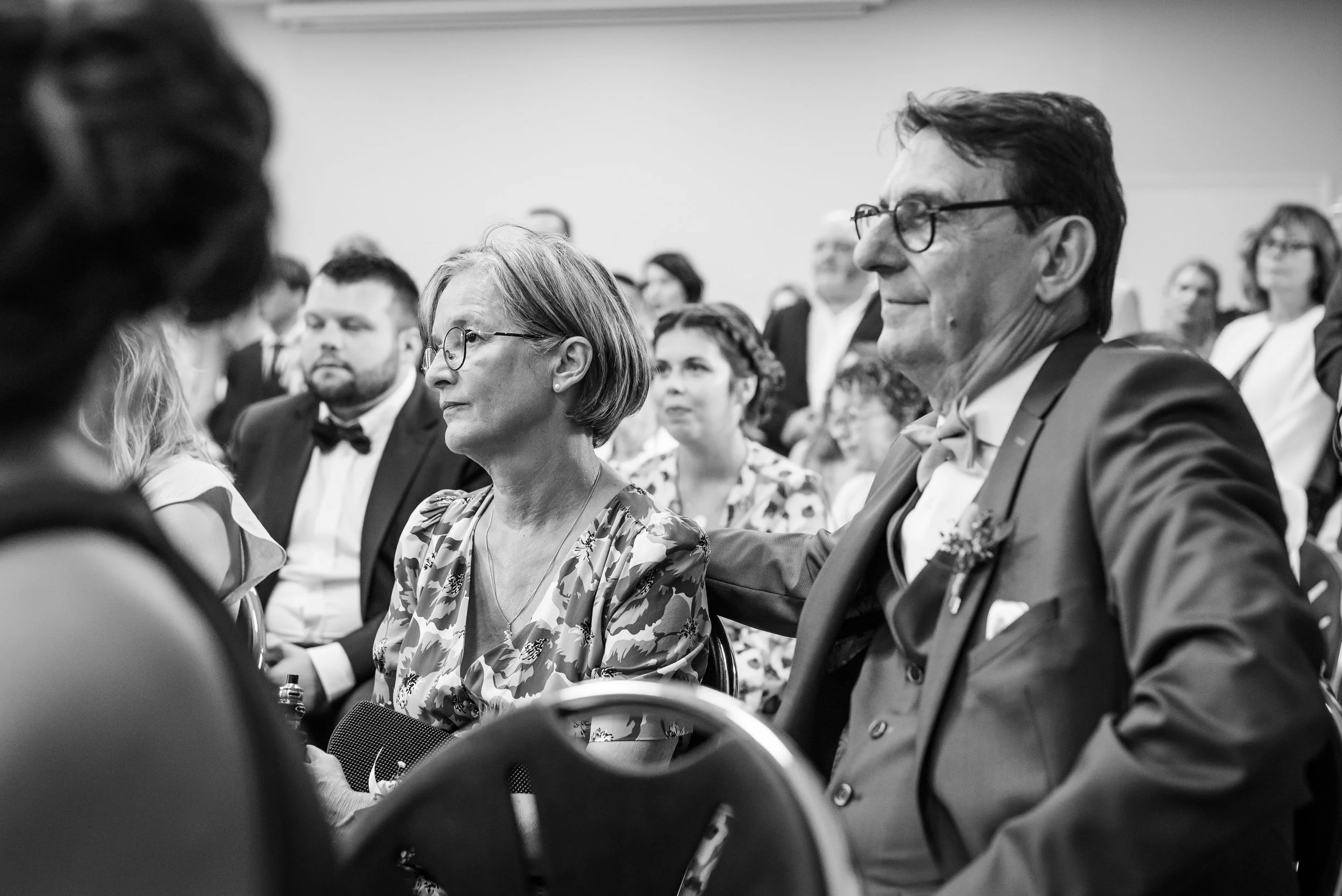 Audience assise lors d'un événement, hommes et femmes en tenue formelle, certains porteurs de lunettes, dans une salle