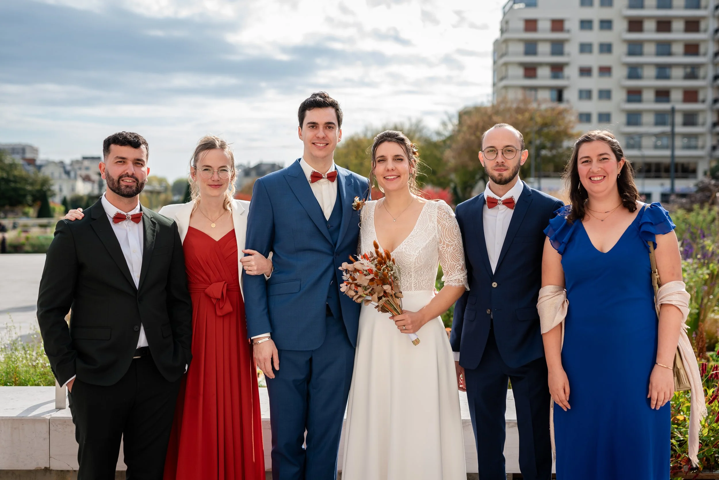 Photo de groupe de six personnes en tenue de soirée, posant dehors devant un immeuble résidentiel, lors d'une occasion spéciale, probablement un mariage.