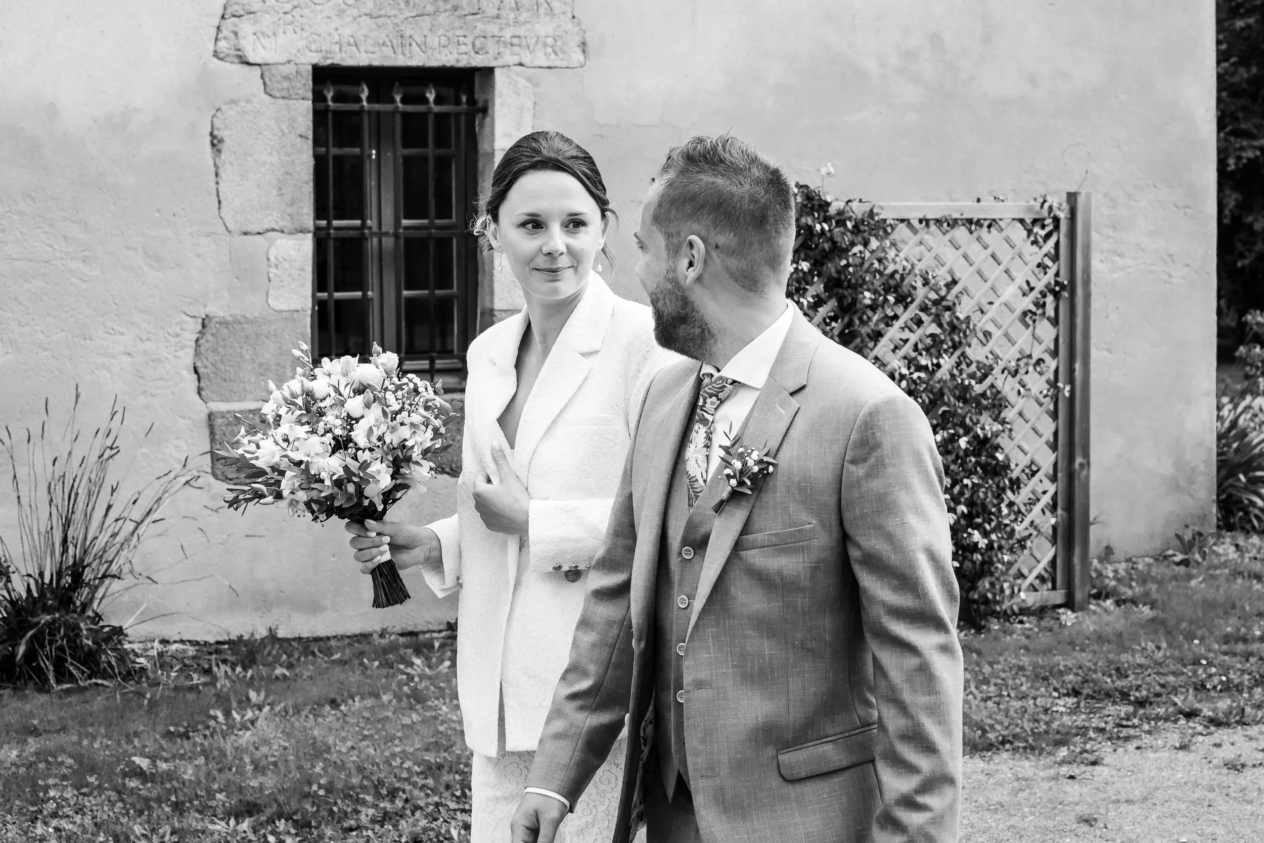 Un couple lors d'un mariage, la femme tenant un bouquet de fleurs et l'homme en costume, en conversation, en extérieur