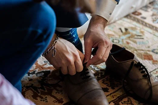 Une personne attache les lacets de ses chaussures en cuir marron sur un tapis.