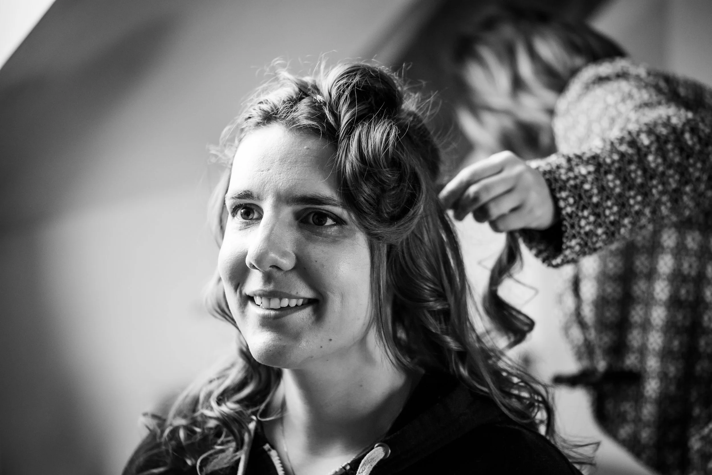 Une femme souriante avec des cheveux bouclés, lors de la séance de coiffure, en noir et blanc.