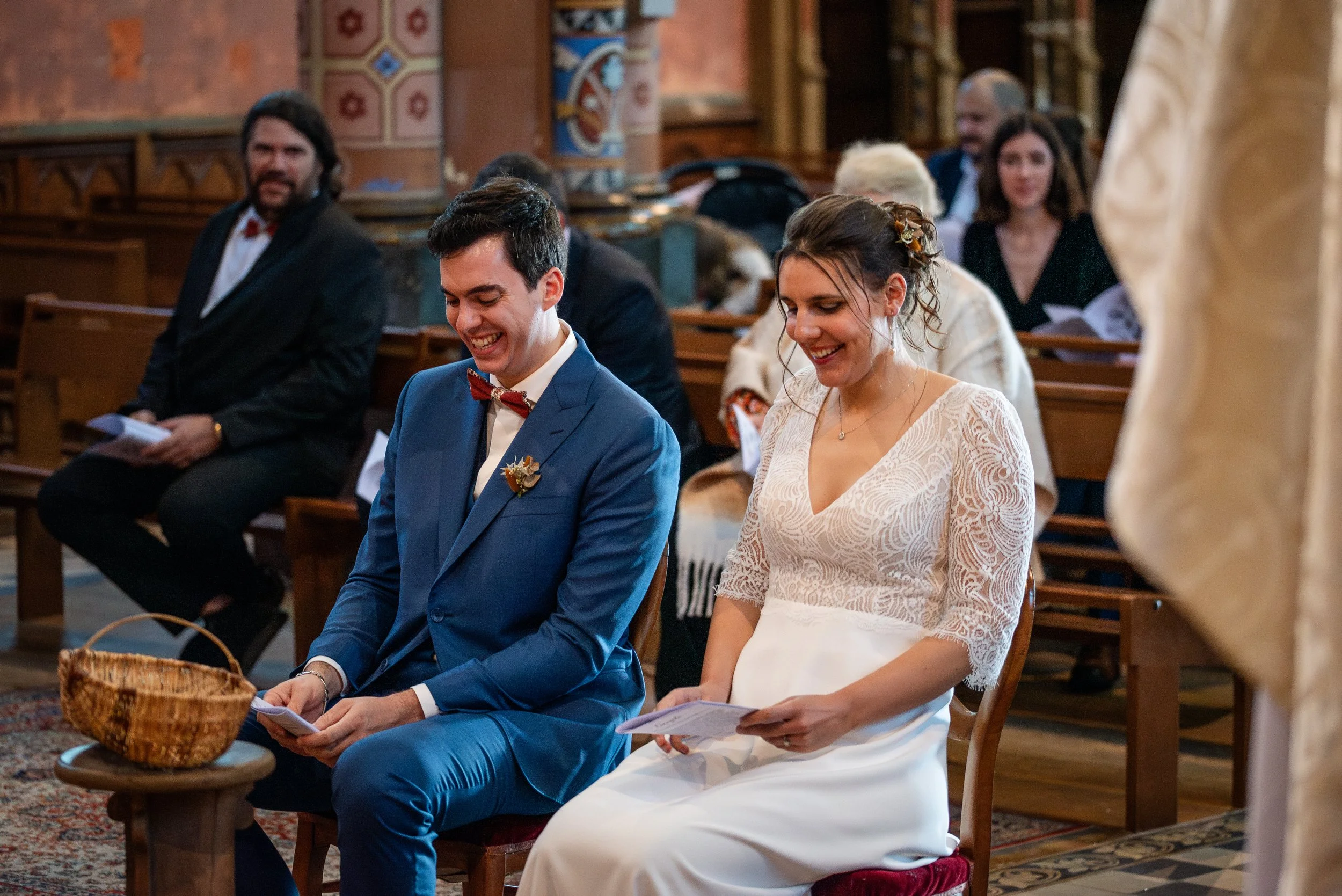 Un couple lors d'un mariage religieux dans une église, assis côte à côte, souriant et tenant des documents en main.