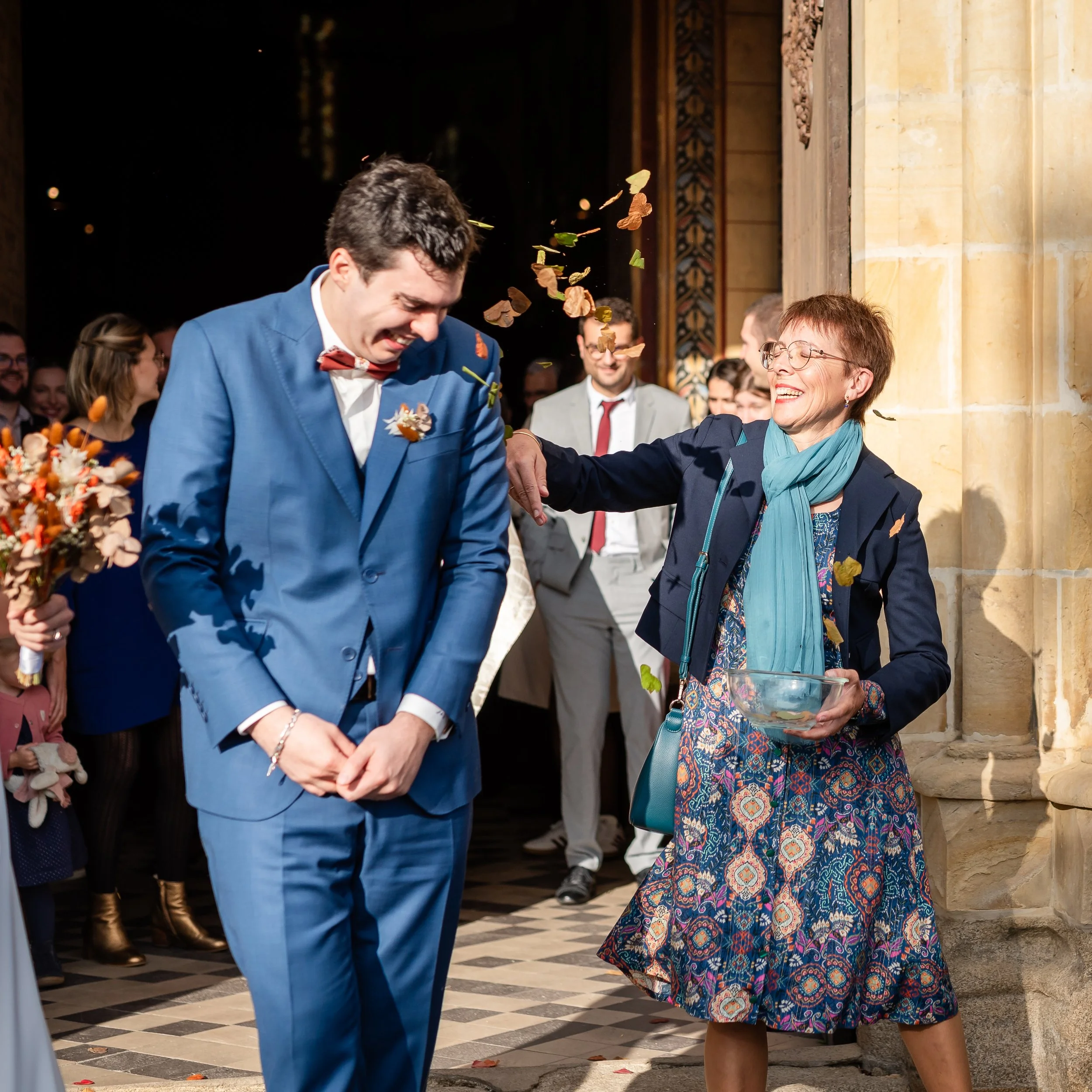 Deux personnes, un homme en costume bleu et une femme en robe colorée, se saluant lors d'une cérémonie à l'intérieur d'une bâtisse historique.