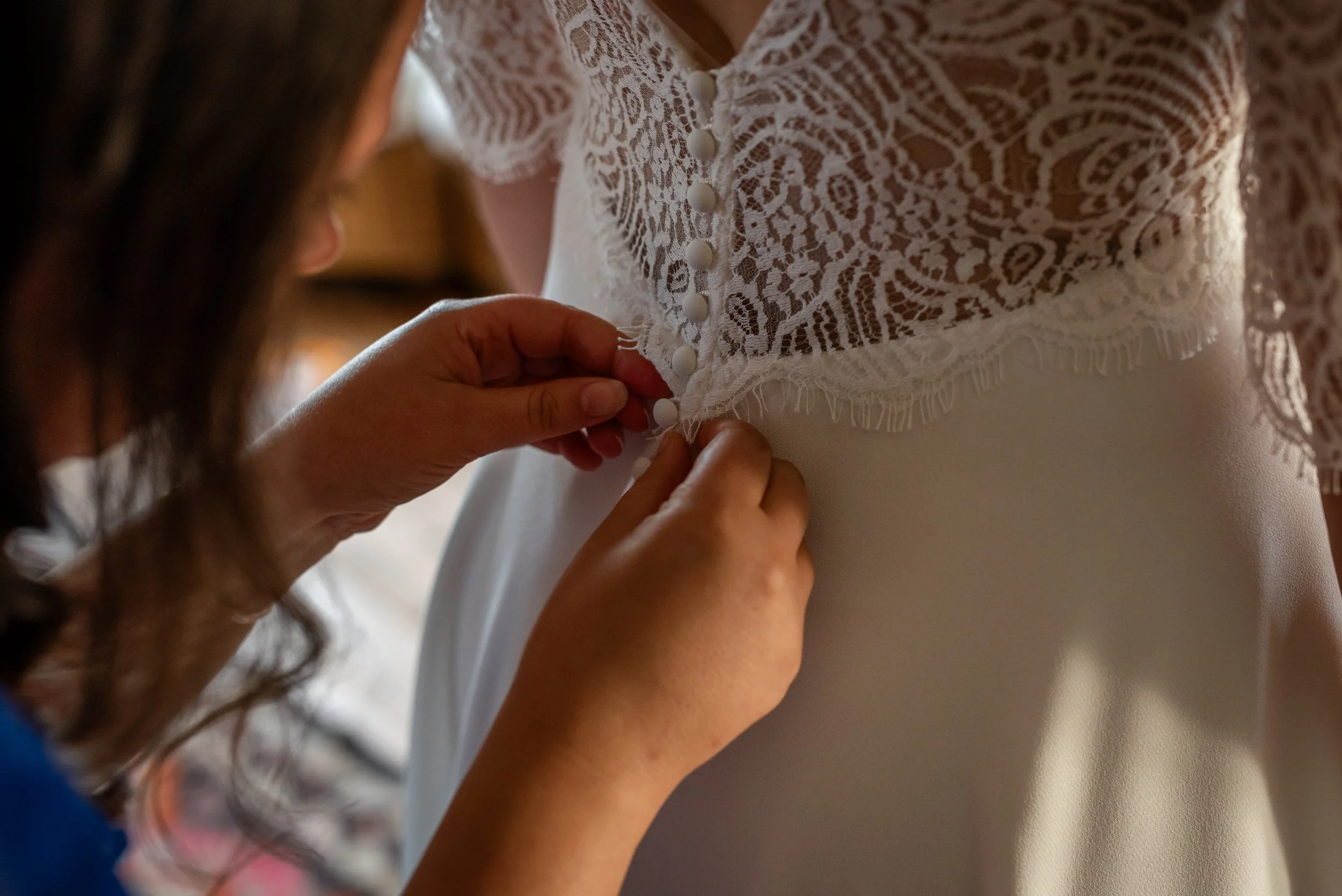 Une personne ajuste les boutons recouverts de dentelle de la robe de mariage d'une autre personne.