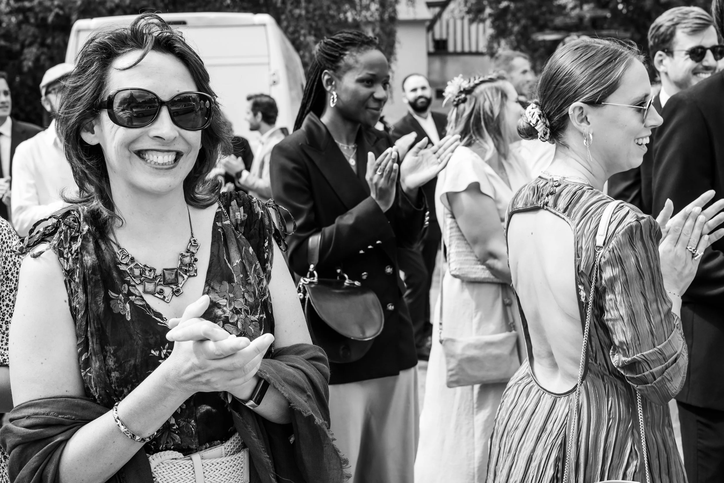 Groupe de personnes regardant dans la même direction, certains souriants et applaudissant lors d'un événement public en plein air, en noir et blanc.