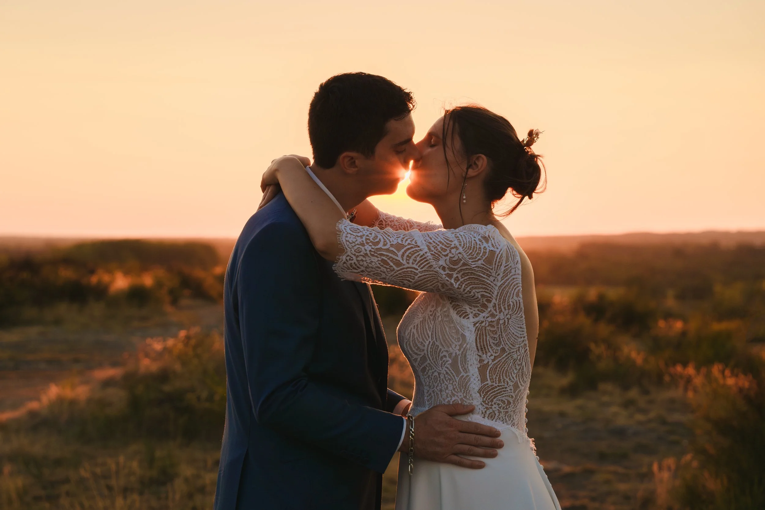 Un couple s'embrasse lors d'un lever ou coucher de soleil à la campagne, avec un ciel orange en arrière-plan.