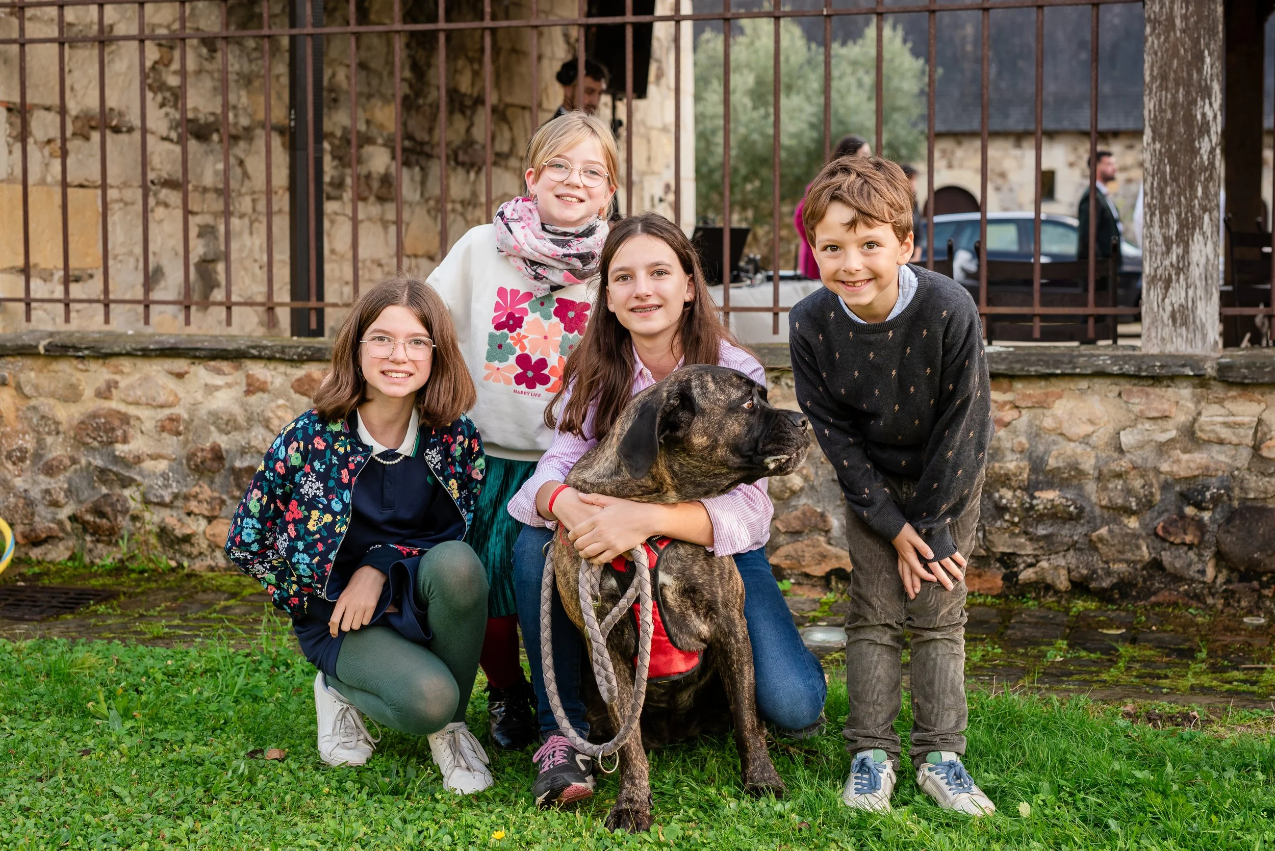 Groupe d'enfants avec un chien, posant devant un mur en pierre, dans un parc ou un jardin pendant une journée ensoleillée.