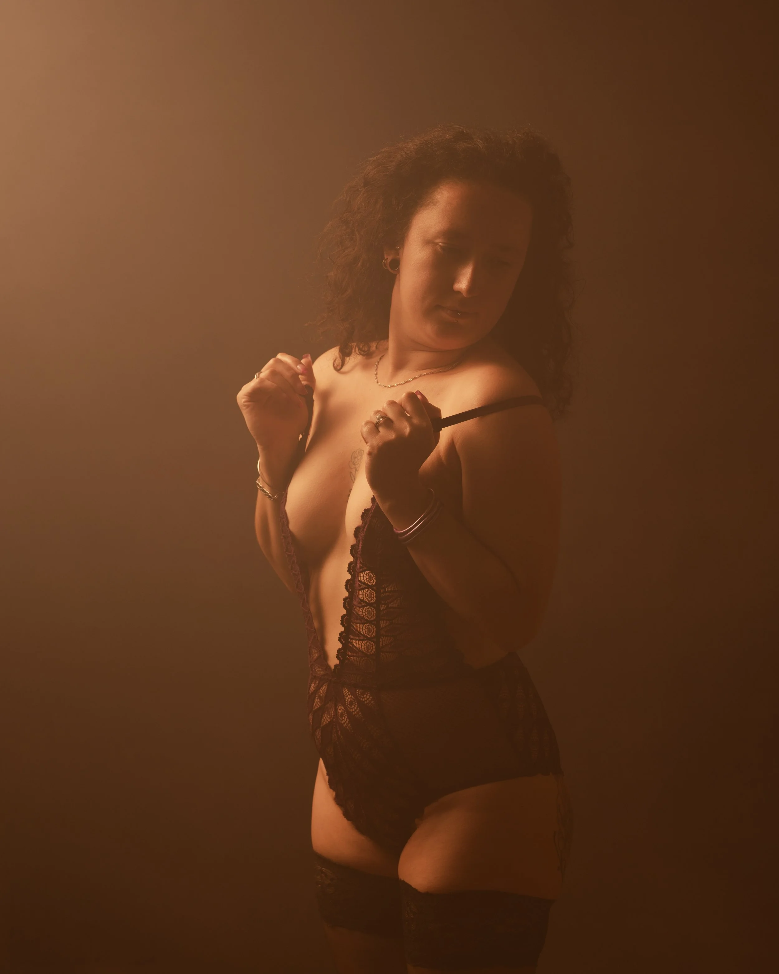 Une femme portant de la lingerie noire, posant de profil avec un fond brun chaud.