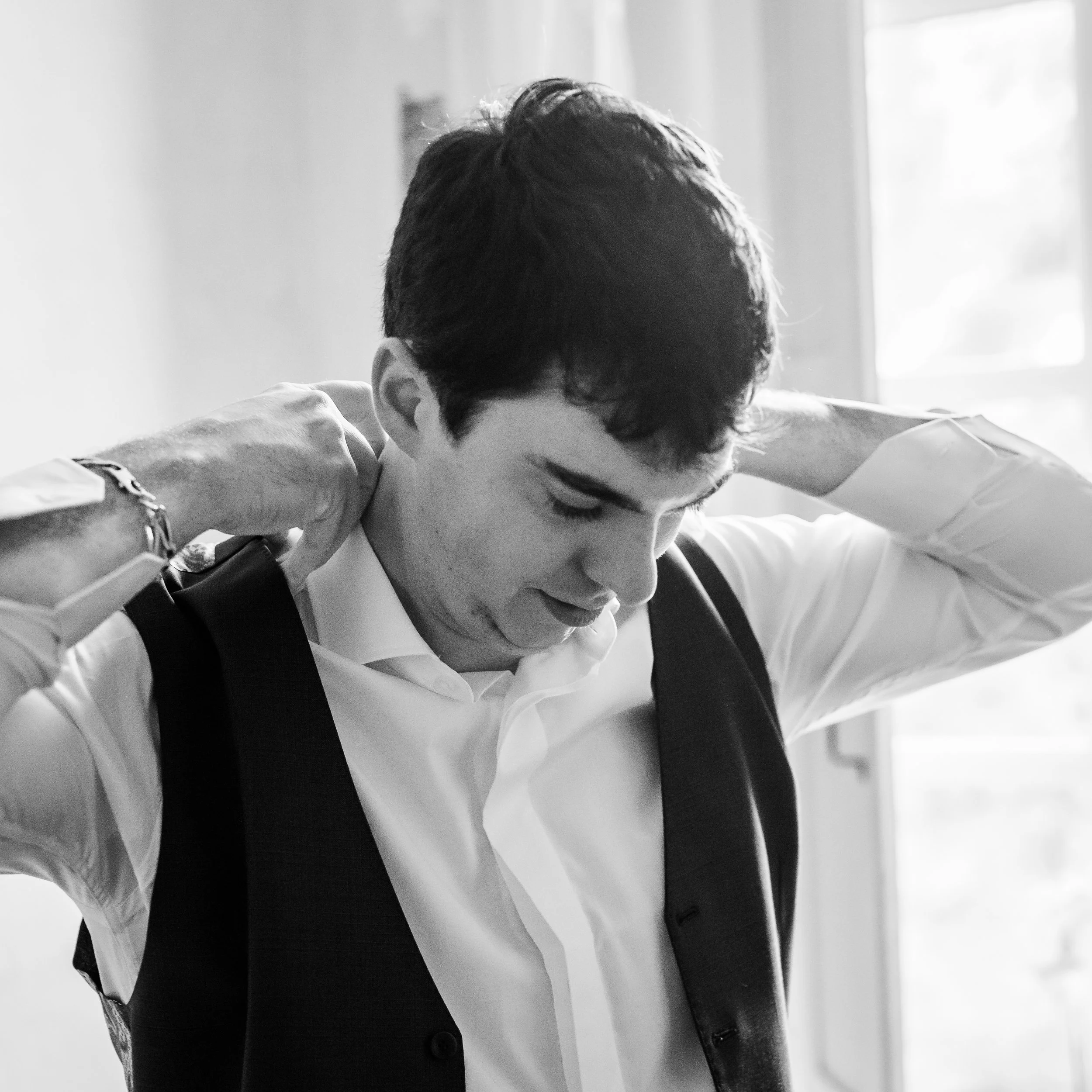 Un homme en costume blanc avec un revers noir et une montre regarde vers le bas dans une pièce lumineuse.