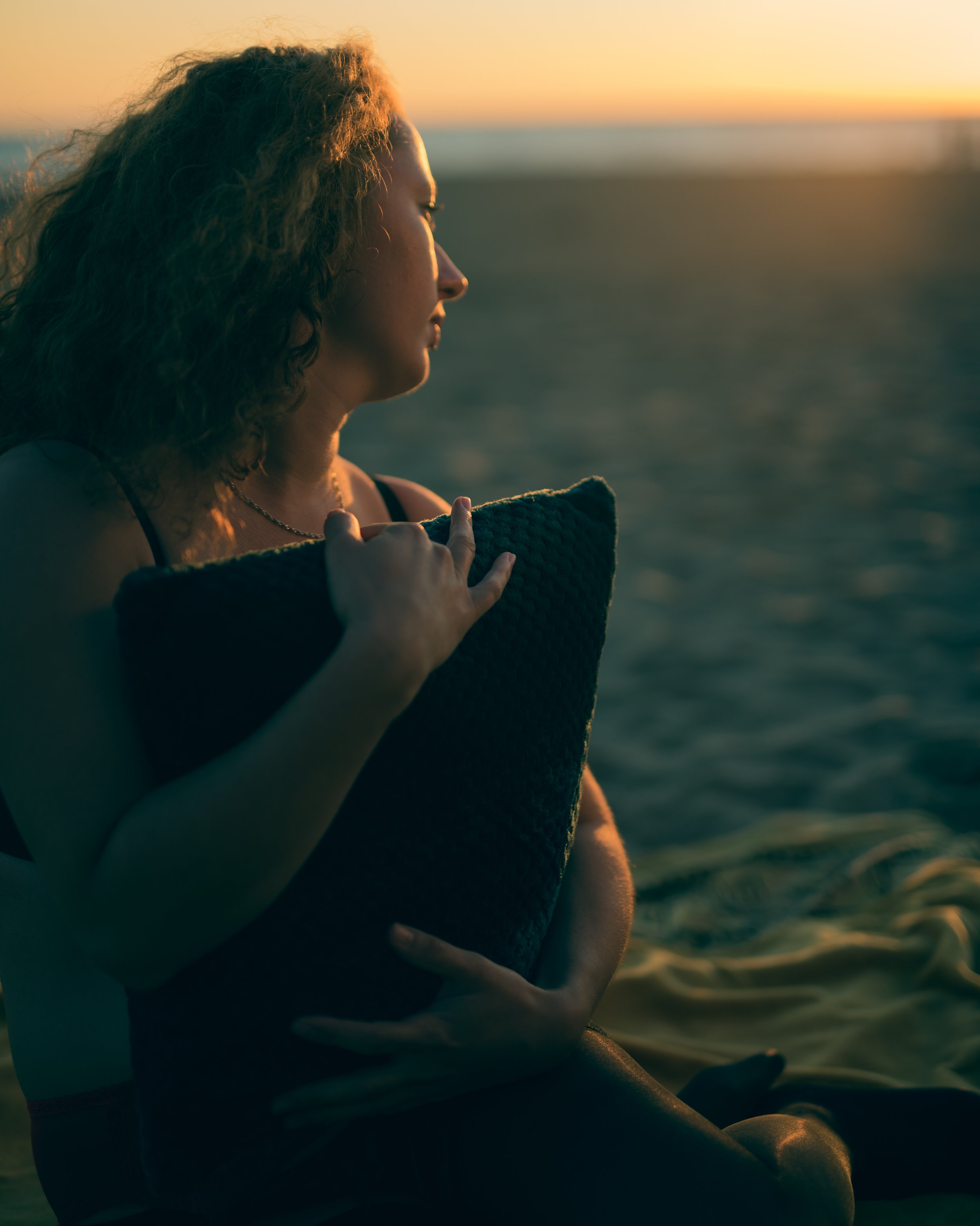 Une femme regarde vers l'horizon au coucher de soleil sur la plage.