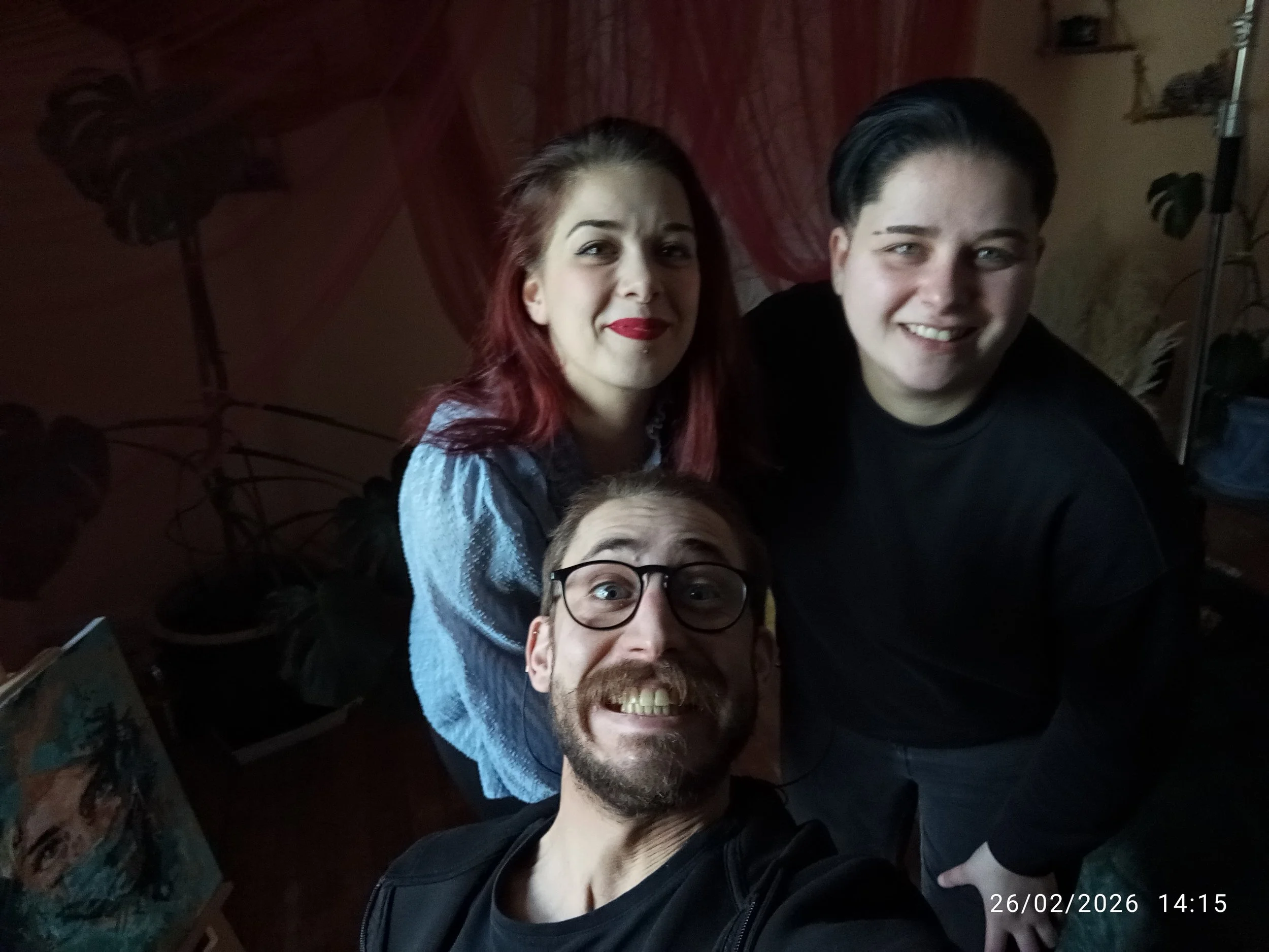 Groupe de personnes souriantes en selfie dans une pièce sombre, avec un arrière-plan de meubles et de plantes. La date et l'heure en bas à droite : 26/02/2026 14:15.