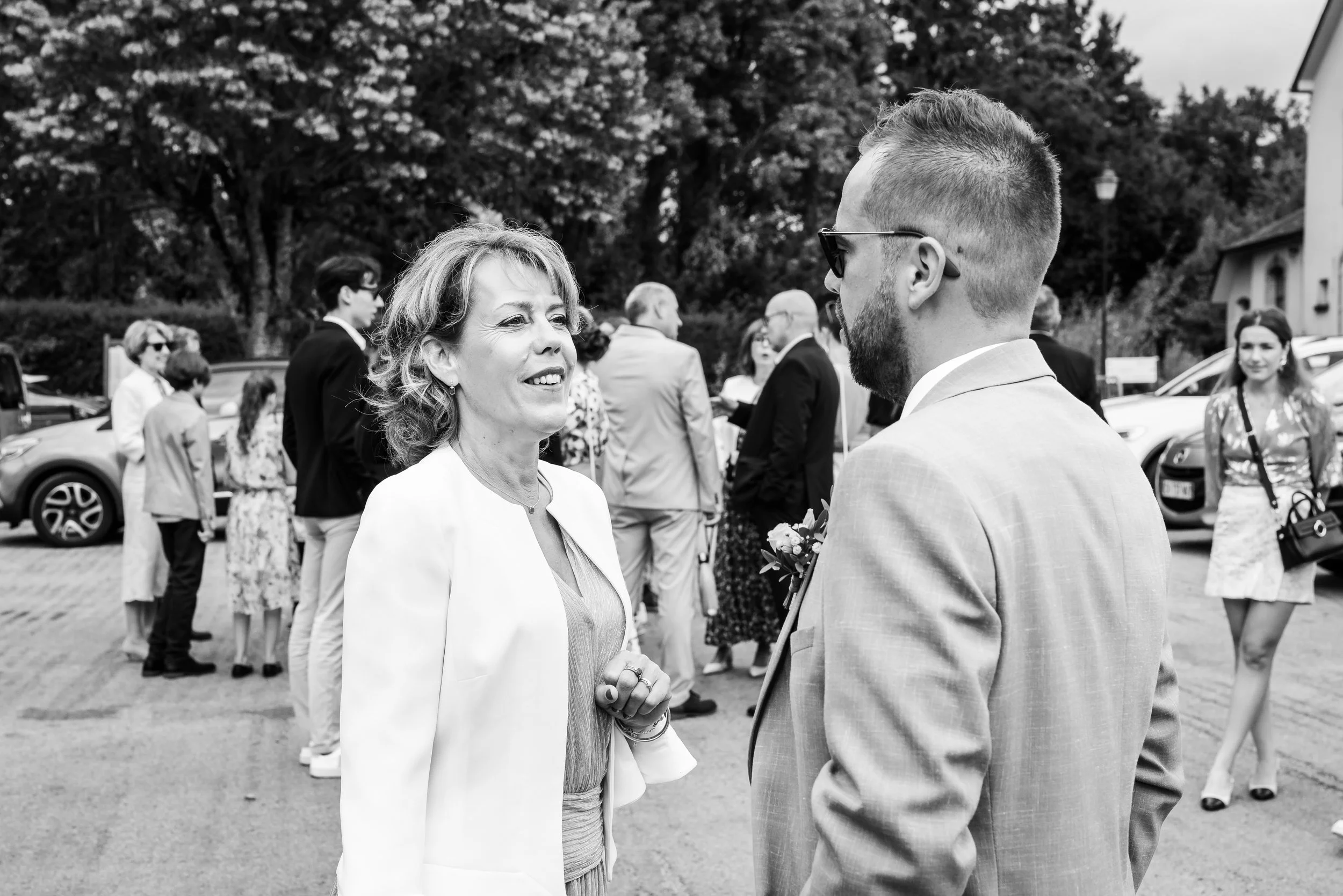 Une femme et un homme discutent lors d'une cérémonie en plein air, entourés de plusieurs autres personnes en arrière-plan.