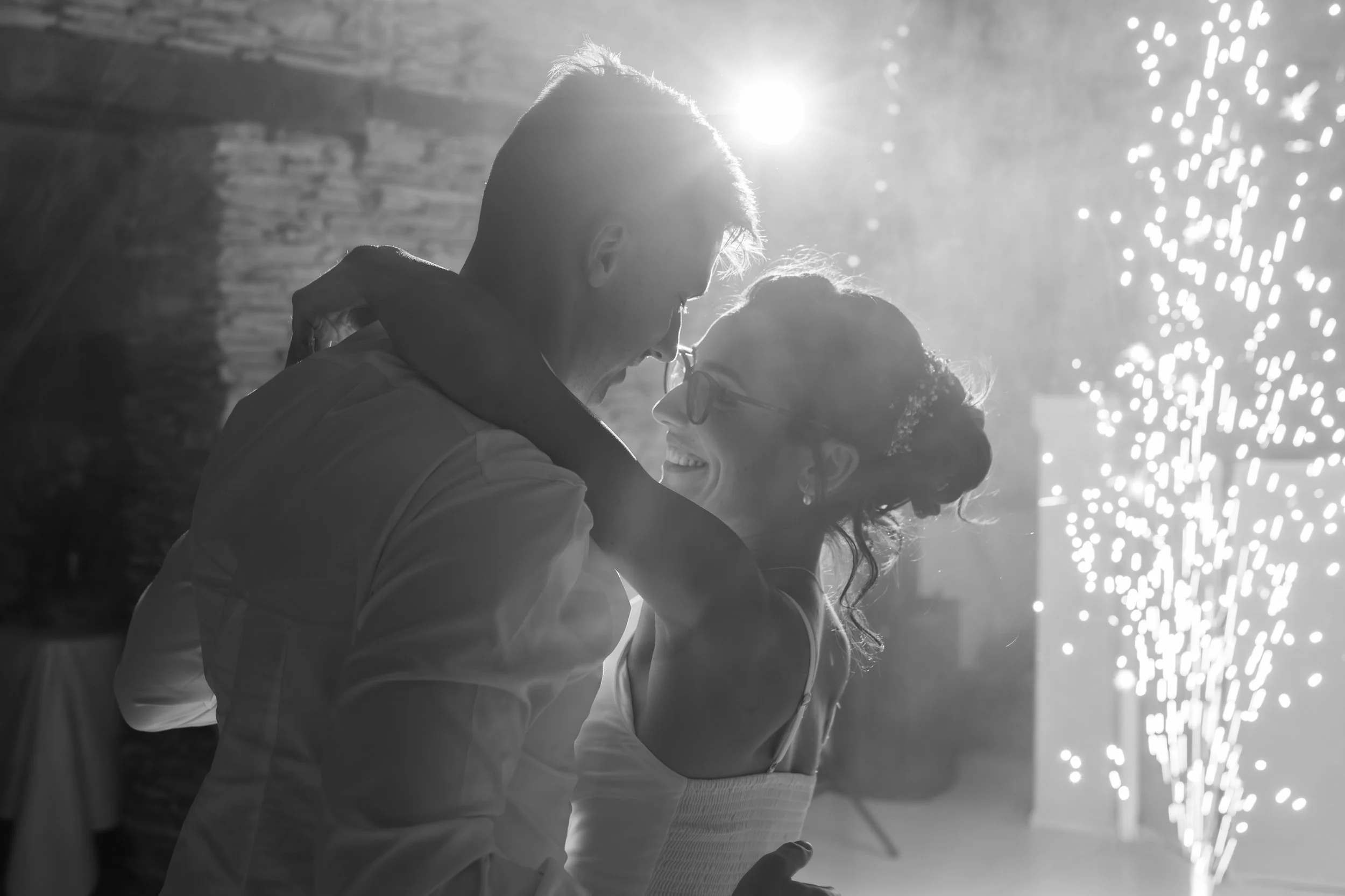 Un couple souriant et fidèle, partageant un moment intime dans une ambiance lumineuse, avec des feux d'artifice en arrière-plan.