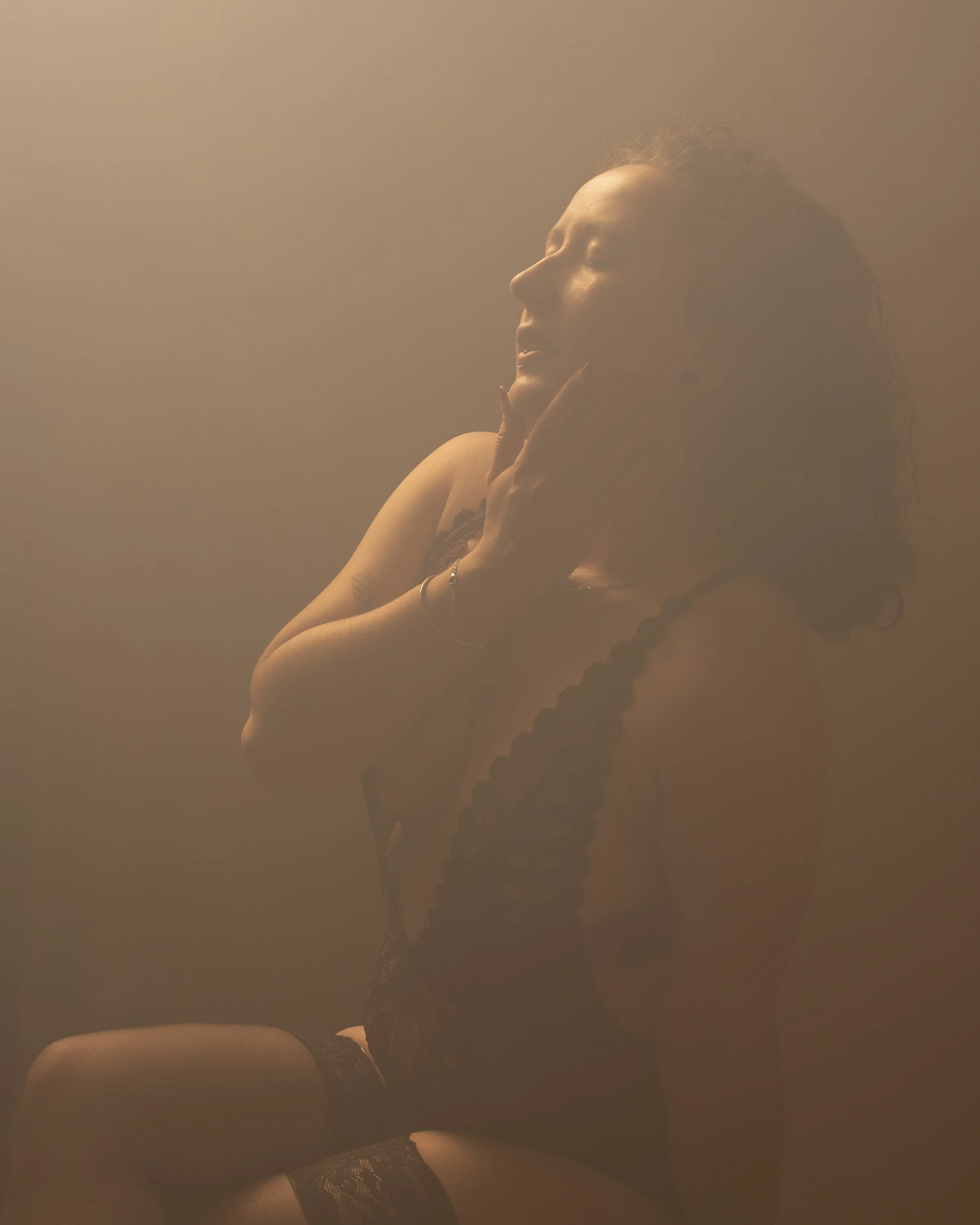 Une femme avec les yeux fermés, portant des collants en dentelle noir, en position contemplative ou relaxée, avec un éclairage doux.