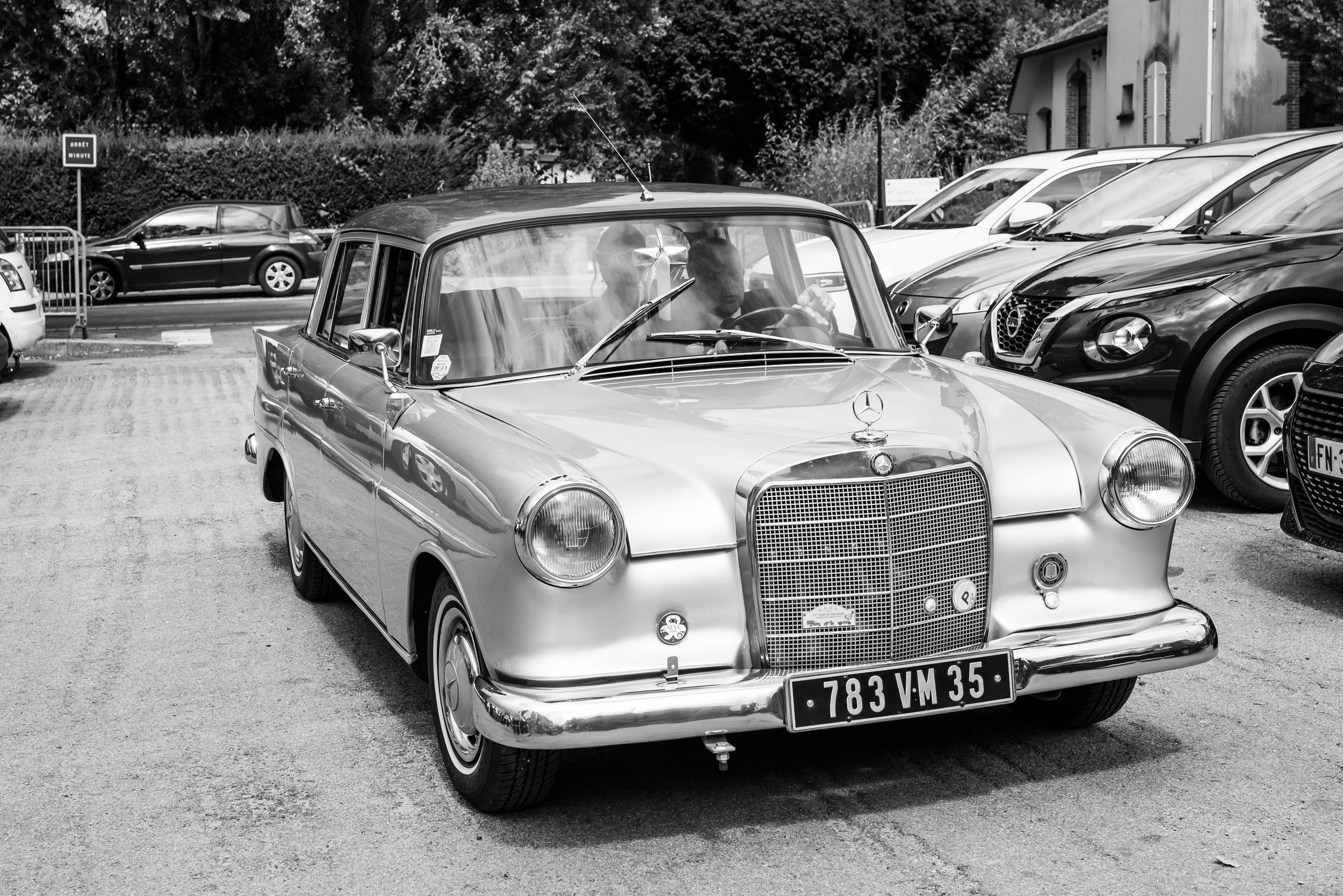 Une voiture vintage Mercedes-Benz garée dans un parking avec d'autres voitures modernes en arrière-plan.