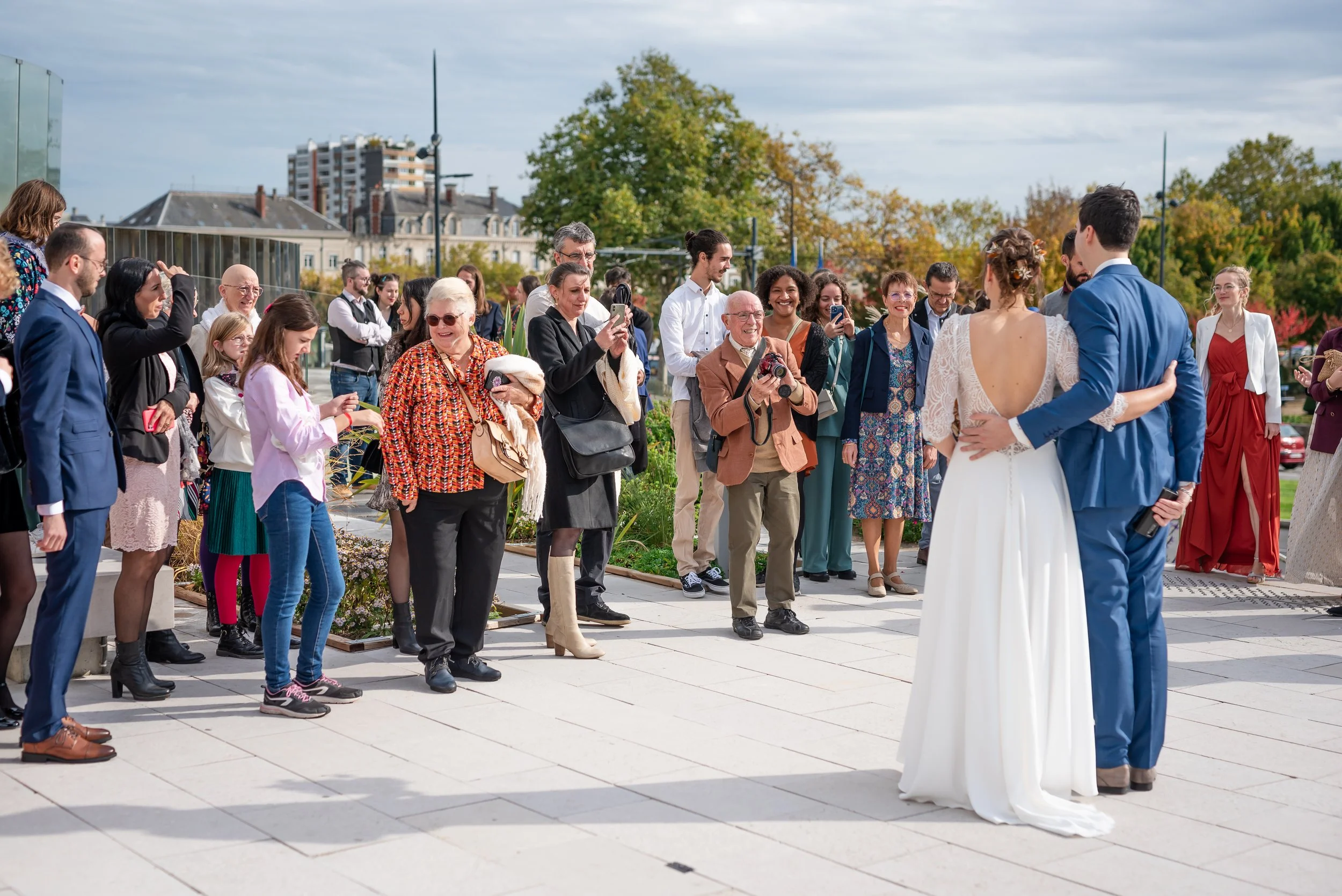 Un groupe de personnes regarde un couple de mariés lors d'une cérémonie en extérieur, en automne.