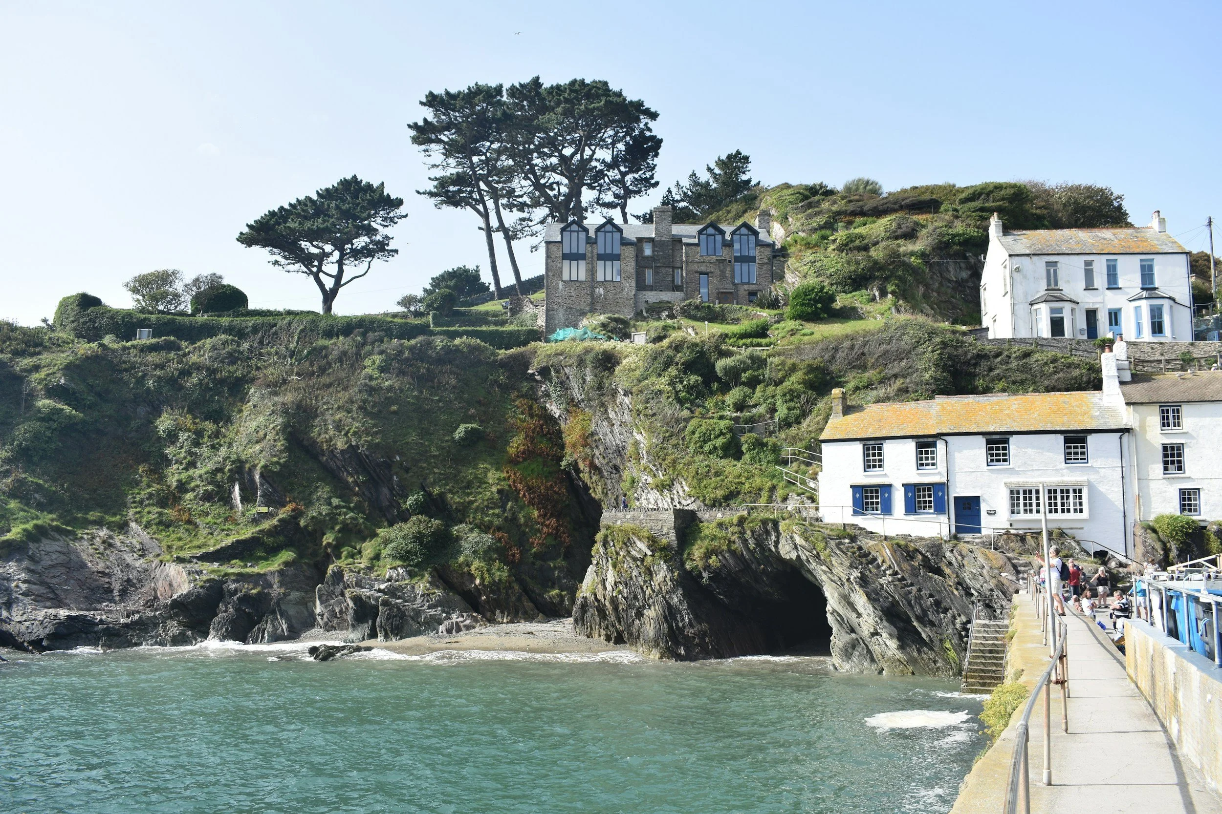 Cliffside houses overlooking the ocean with a walkway and people near the water.