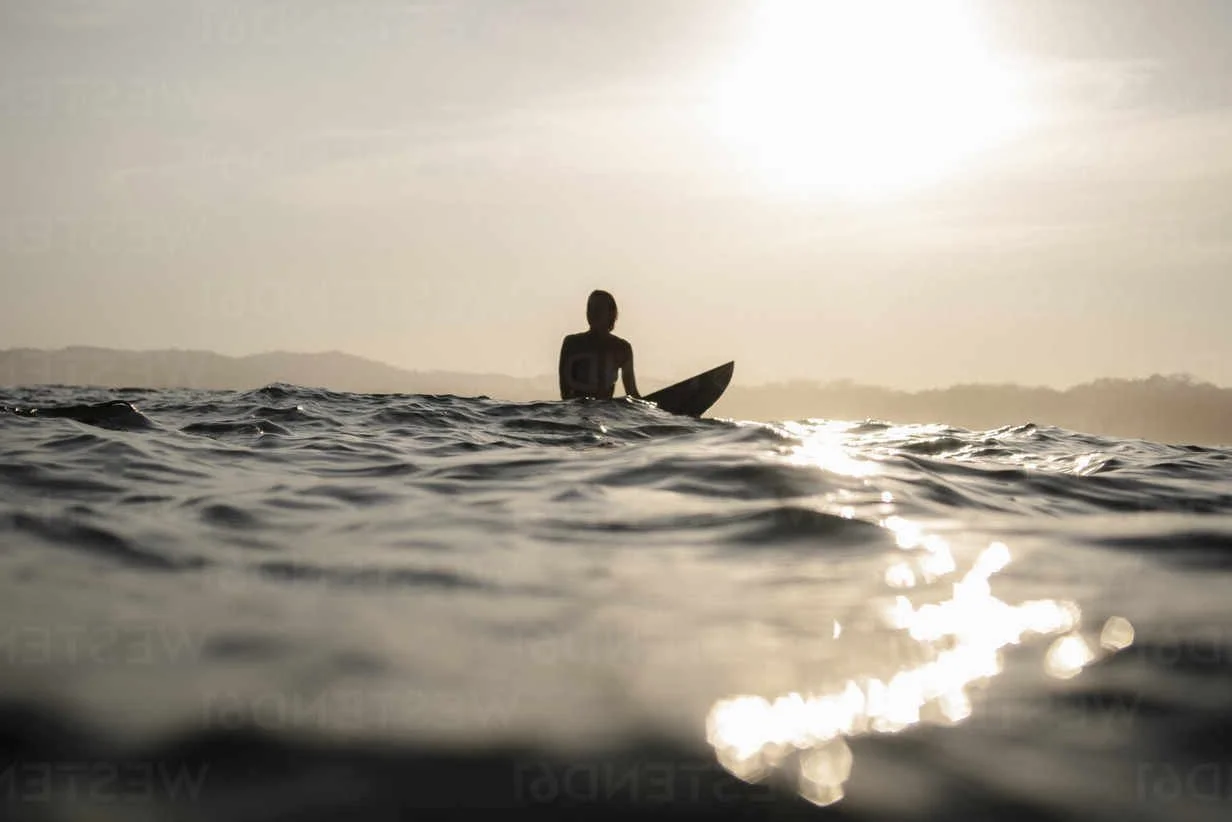 female-surfer-sitting-on-surfboard-in-the-evening-costa-rica-HWHF00016.jpg
