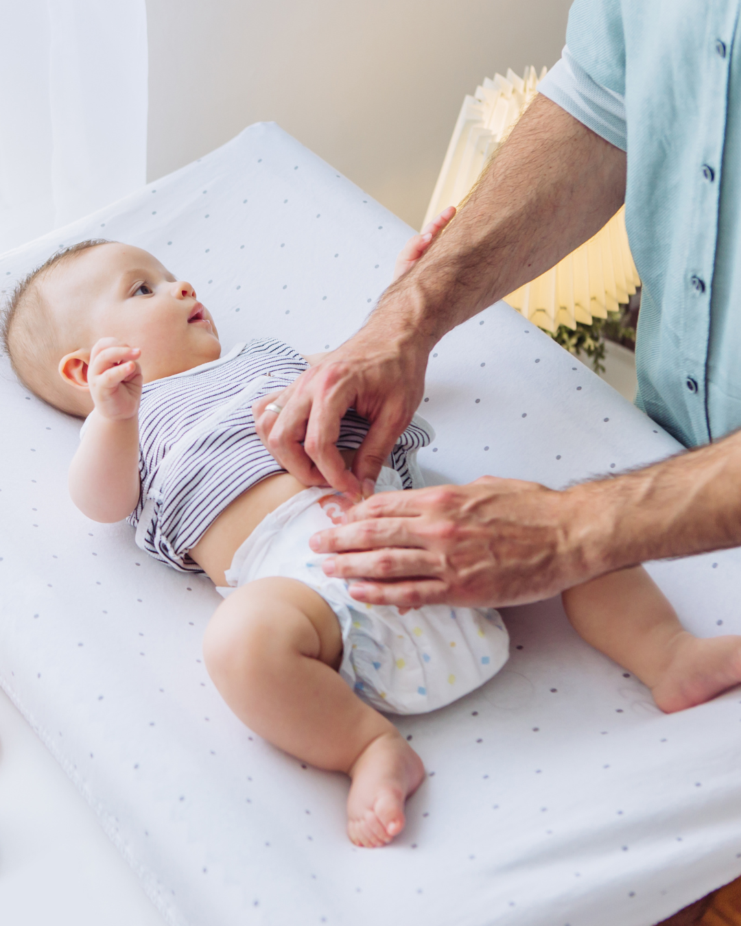 A newborn baby lying on a changing table being diapered by an adult male figure.