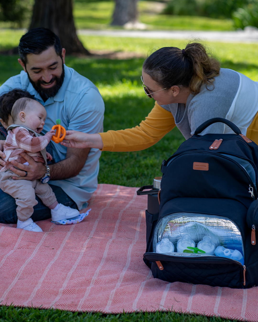 Day Trip Diaper Bag backpack family at the park with a picnic setting on a blanket