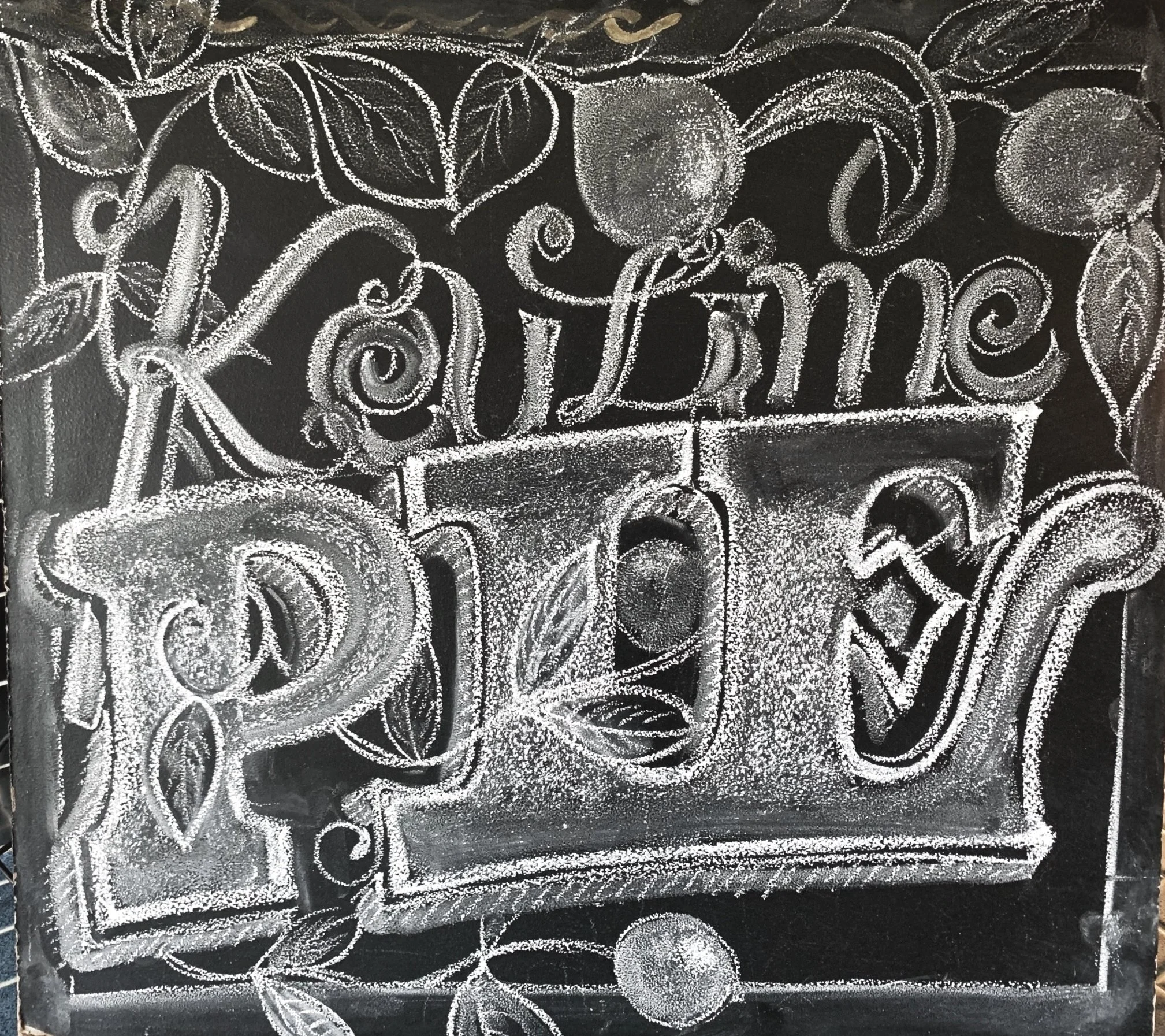 Chalkboard sign with the message "KaLime PINK" written in decorative script, surrounded by drawings of leaves and lemons, against a tiled wall background.