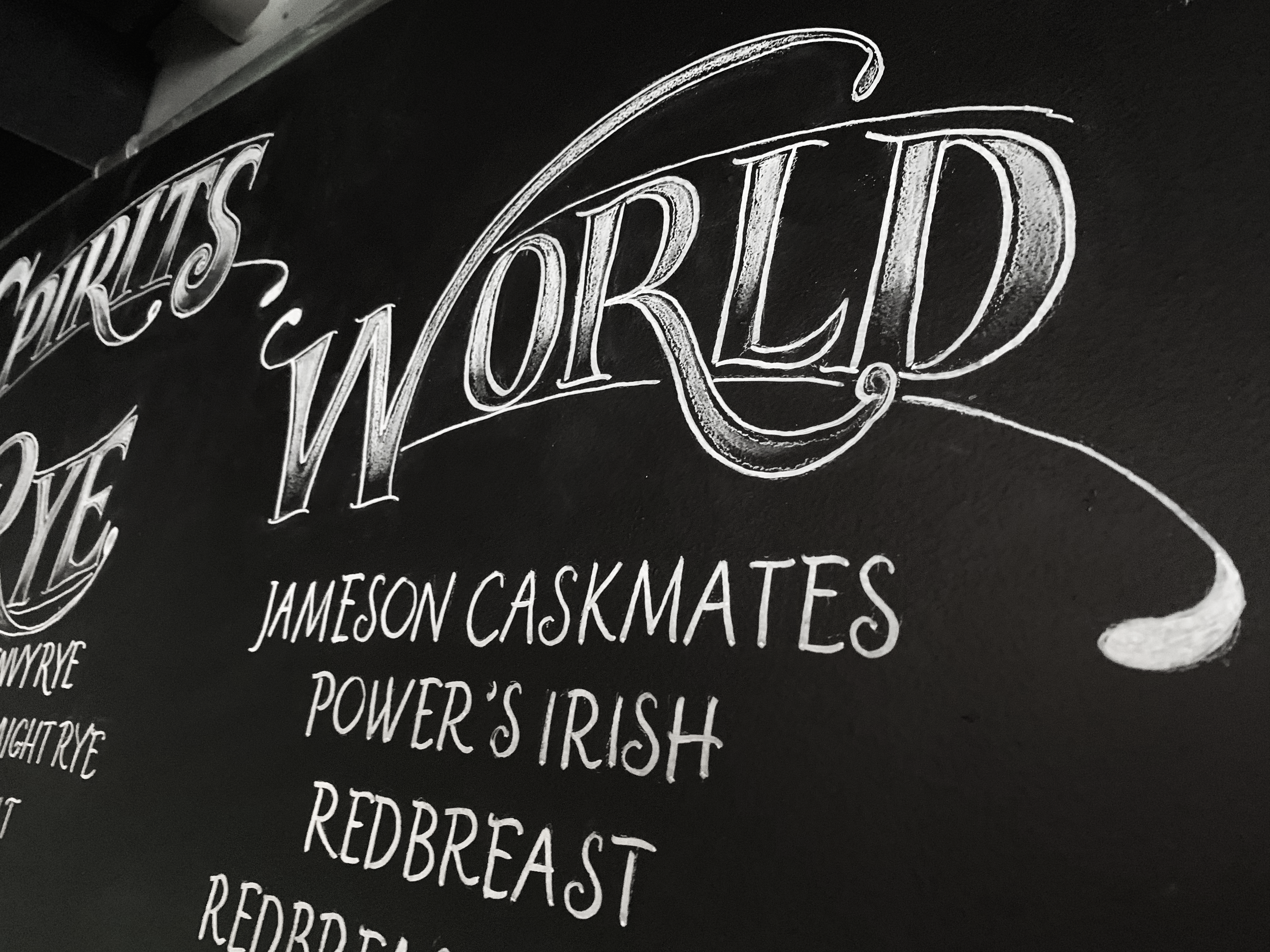 Chalkboard menu with decorative text reading 'In the World' and listed dishes such as Jameson Caskmates, Power's Irish, Redbreast, and Red. The menu is written in white chalk on a blackboard.