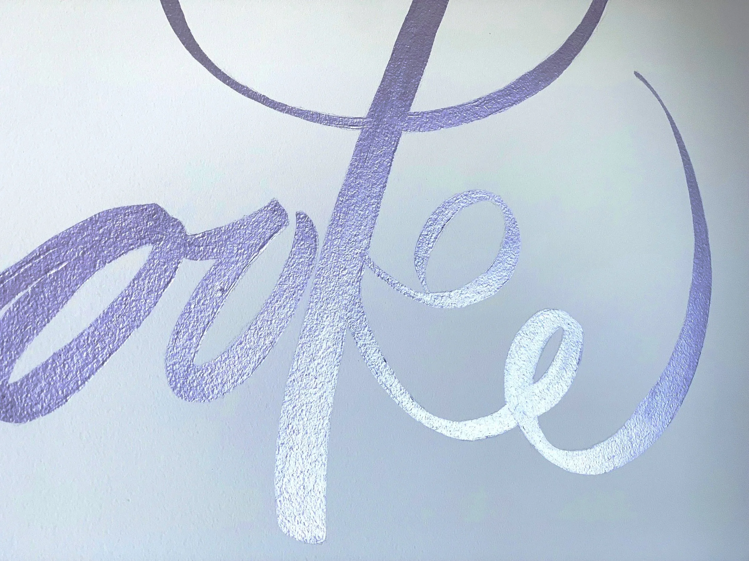 Close-up of a word written in a glittery, purple cursive font on a white background.