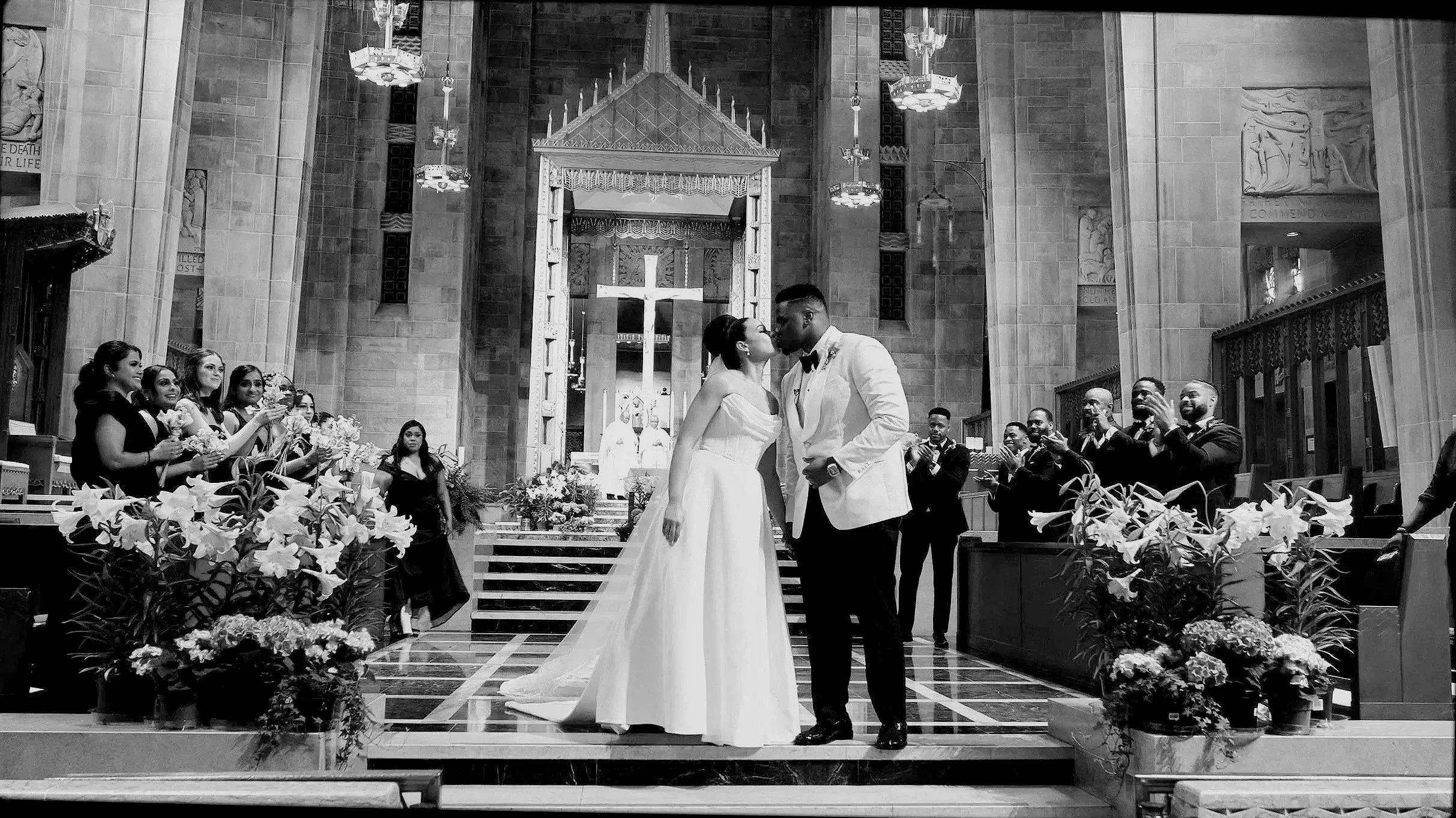 A wedding ceremony inside a church with the bride and groom kissing at the altar, surrounded by wedding attendants and guests.