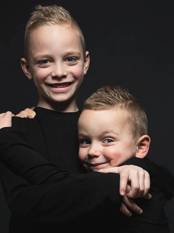Twee lachende jonge jongens die elkaar knuffelen, met een donkere achtergrond.
