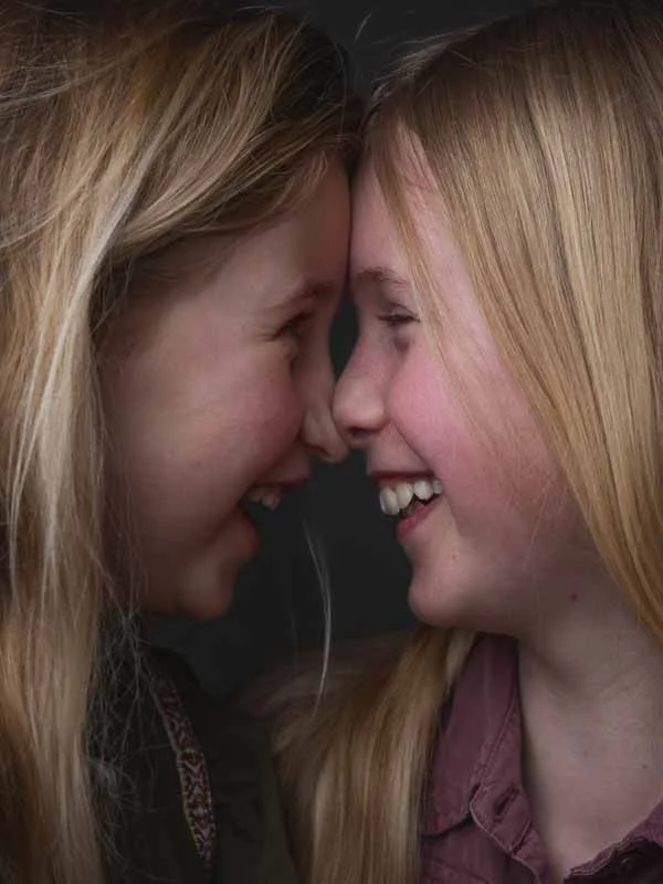 Twee jonge vrouwen lachen en staan heel dicht bij elkaar met voorhoofd tegen voorhoofd, lachend met gesloten ogen.