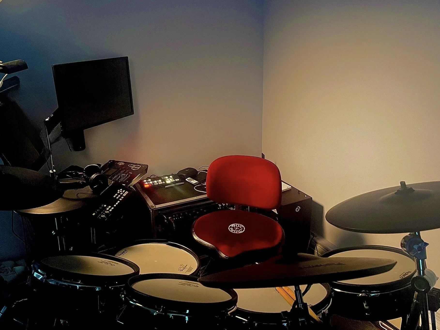A drum studio with electronic drum set, a red chair, and a music mixer.