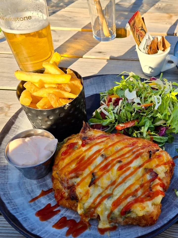 chicken parmo with salad and fries on a table outside a pub
