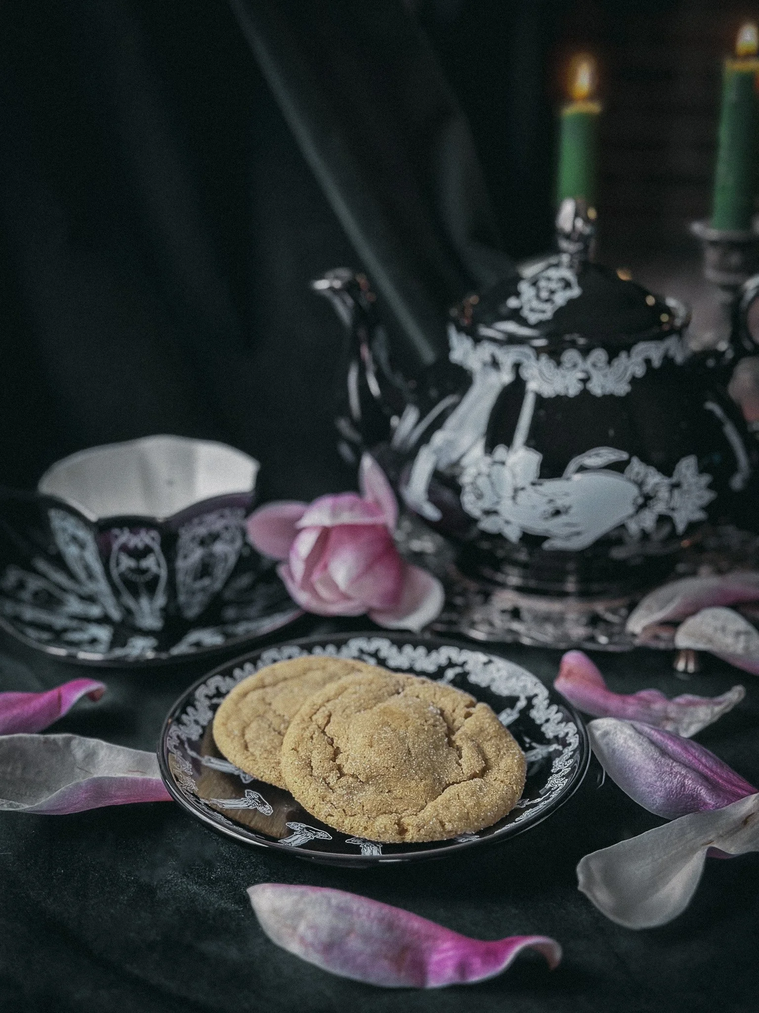 A plate of sugar cookies surrounded by magnolia petals and black and white china.