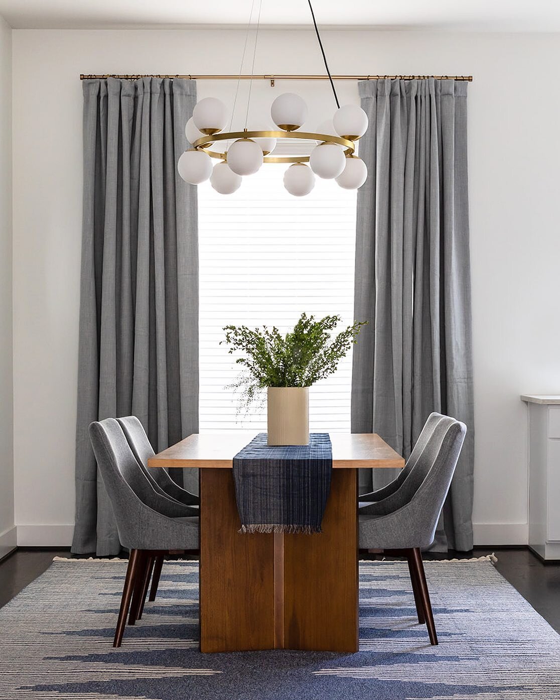 Modern &amp; symmetrical.

Dramatic drapes and a large area rug create a dining &ldquo;room&rdquo; in this open concept dining-kitchen-living space. Layering upholstered chairs, a modern wood table, and a statement chandelier bring it all together! ?