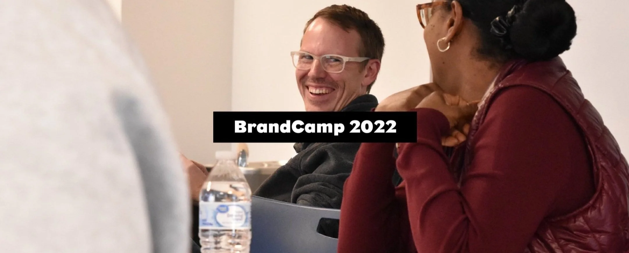 a BrandCamp person in a chair with a bottle of water smiling at another person