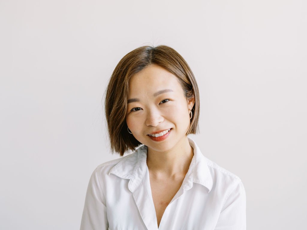 Portrait of a person with shoulder-length brown hair and a white sweater, smiling at the camera.