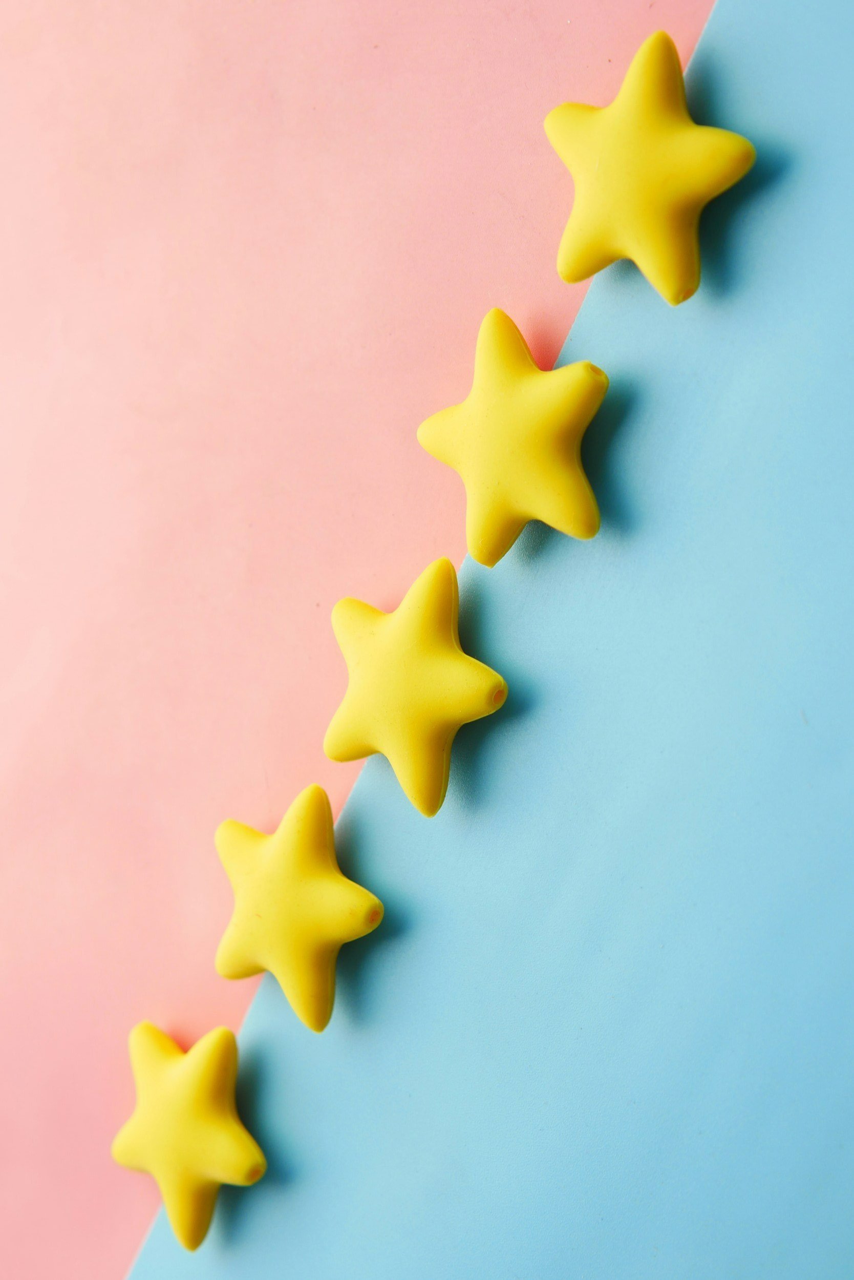 Five yellow star-shaped objects arranged in a diagonal line on a pastel pink and blue background.