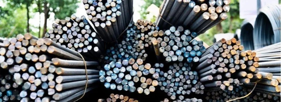 Bundles of metal rods stacked together outdoors, with trees and sky in the background.