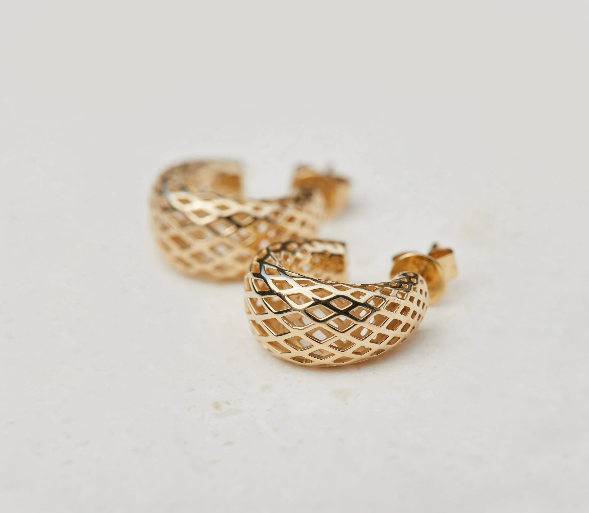 Gold earrings with a geometric open lattice design on a white background.